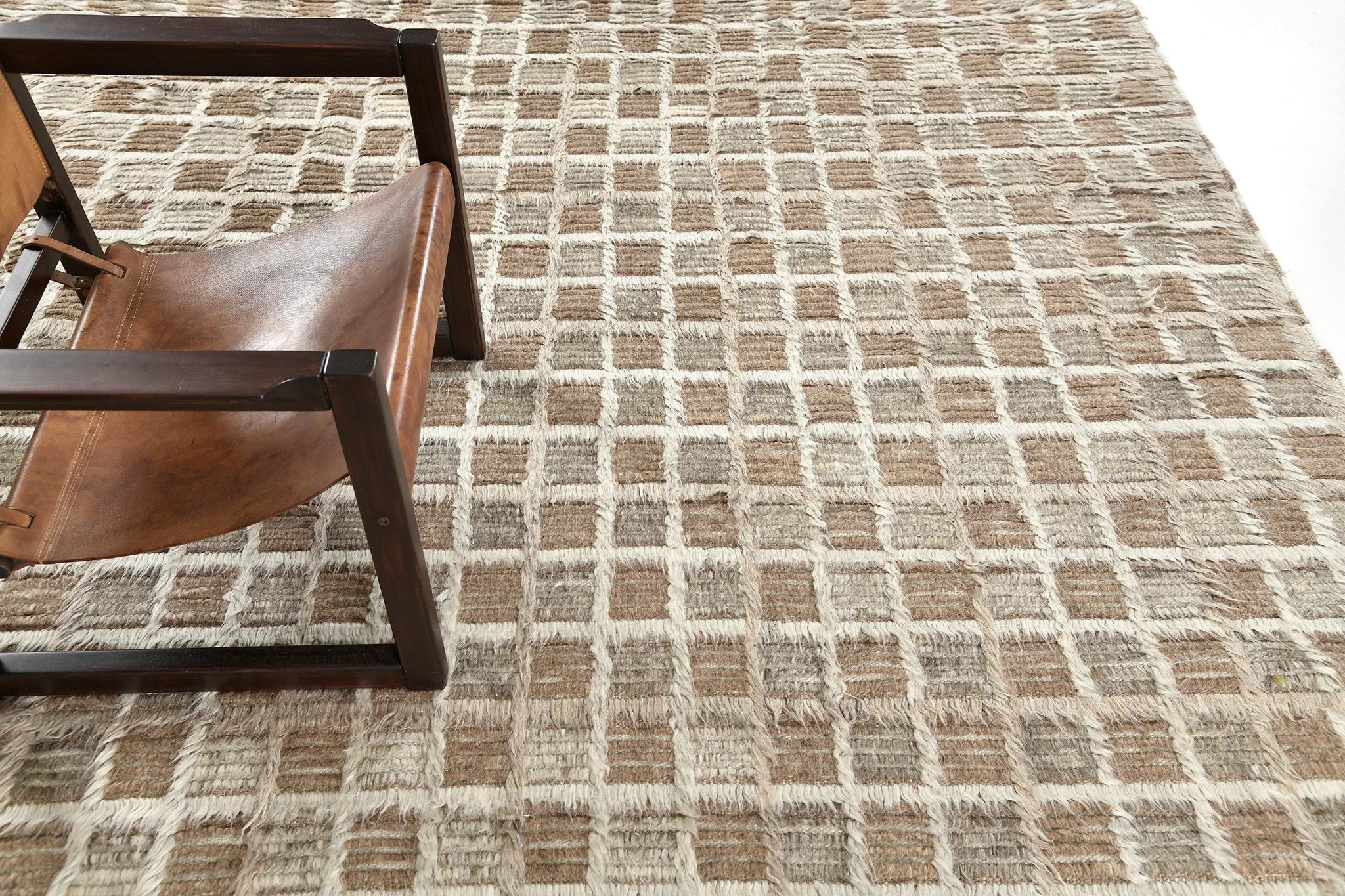 Der Teppich Miha zeichnet sich durch ein Schachbrettmotiv aus, das in einem Mehrflor-Design mit verschobenen, tonalen Gitterlinien spielt. Dieses Stück ist in subtilen Neutraltönen gehalten, die warme Lehmtöne und khakifarbene Grautöne umfassen.