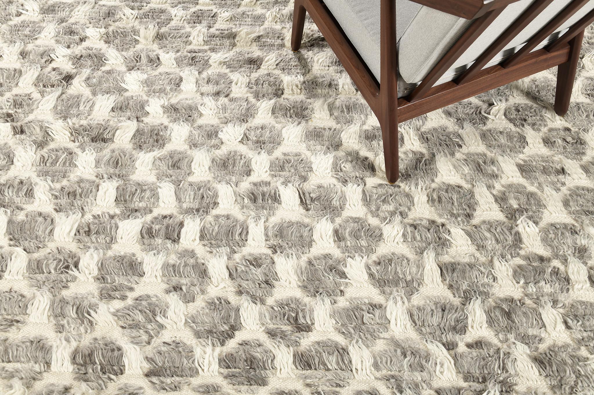 Der Teppich Hanin ist ein komplexes, mehrfarbiges Rastermotiv in langen Florlinien mit Formen von Zierflor und offenen Flachgewebe-Akzenten. Hanin ist mit einer warmen Mischung aus Kakao-, Lehm- und Goldtönen in gemischten Grautönen auf