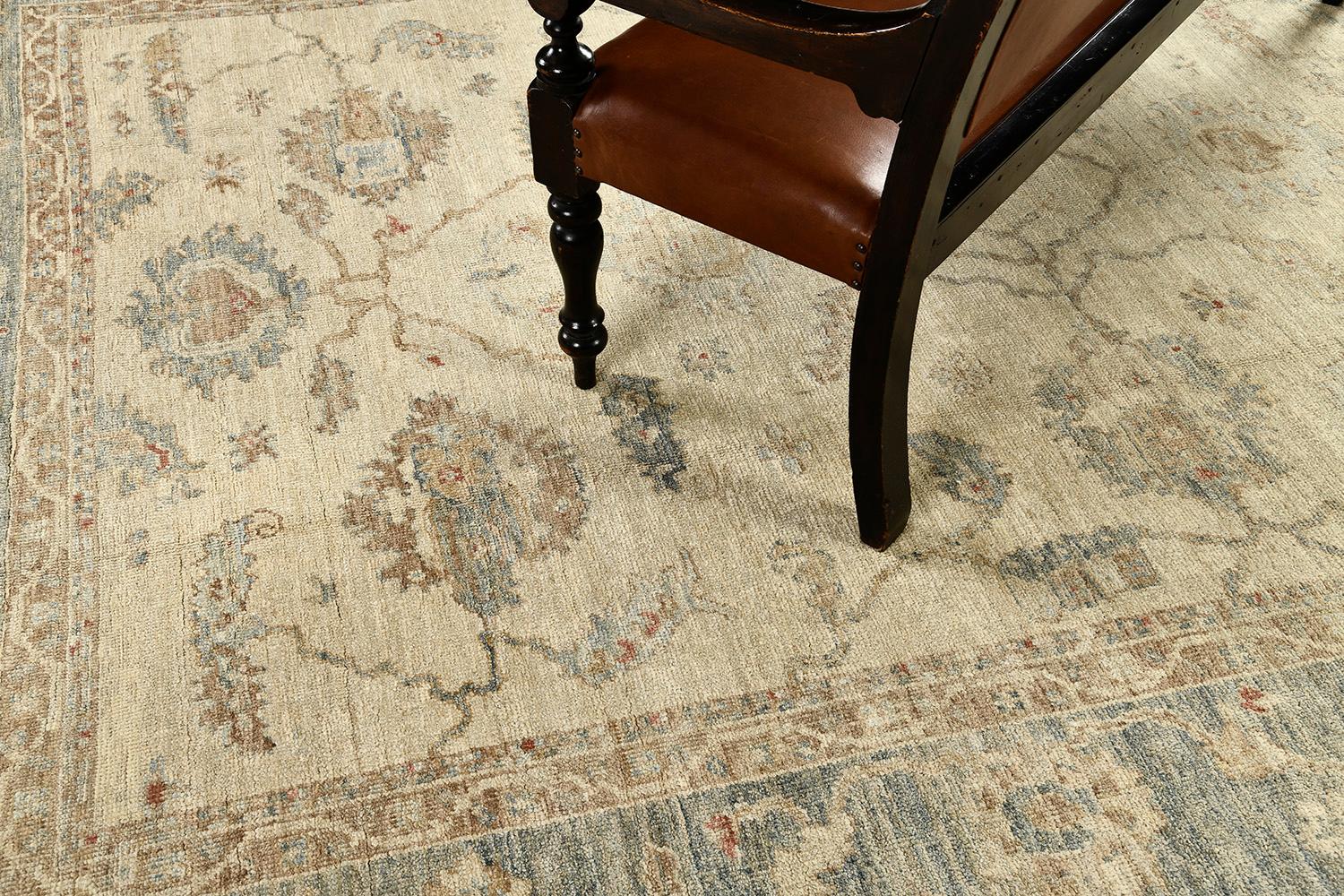 A stylish Oushak revival rug in the muted tones of ivory, sky blue, and burnt sienna defined gracefully with majestic botanical details. Classic, dainty and cozy, this rug from hand-spun wool is framed by a complementary border filled with elements