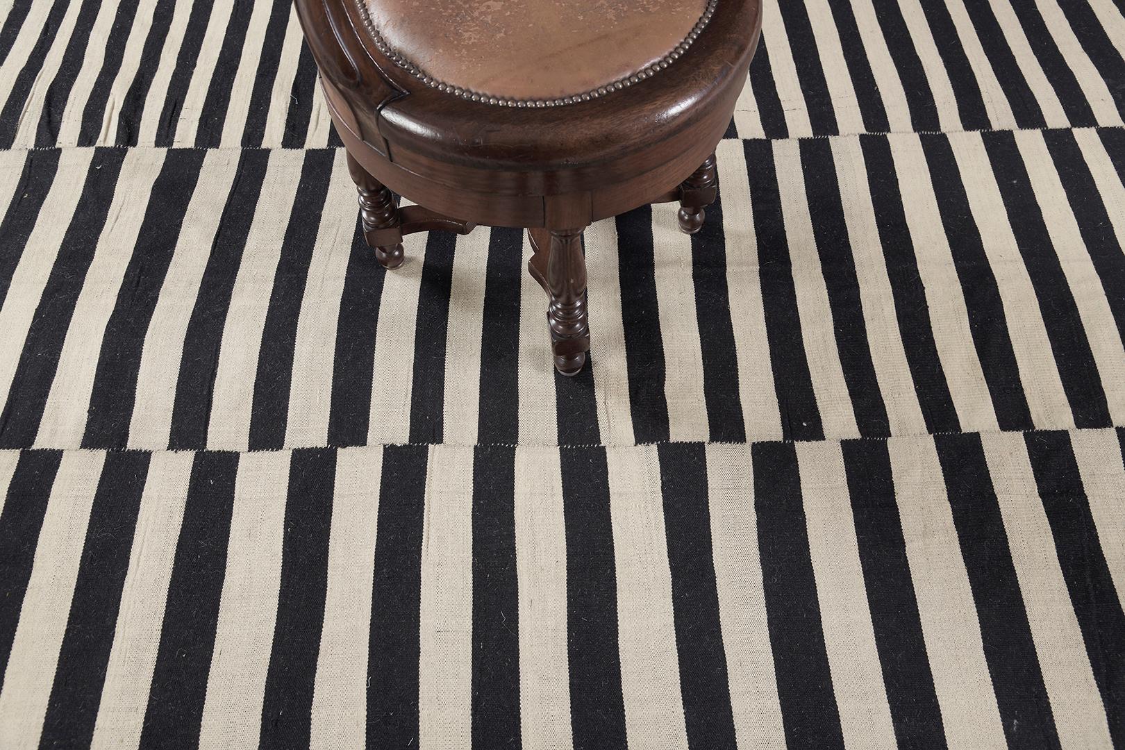 A stunning vintage Persian Kilim flatweave banded with black and neutral palette stripes. The varying degrees of stripes create a modest yet fascinating design for an extensive variety of interiors. A stylishly beautiful masterpiece that your guest
