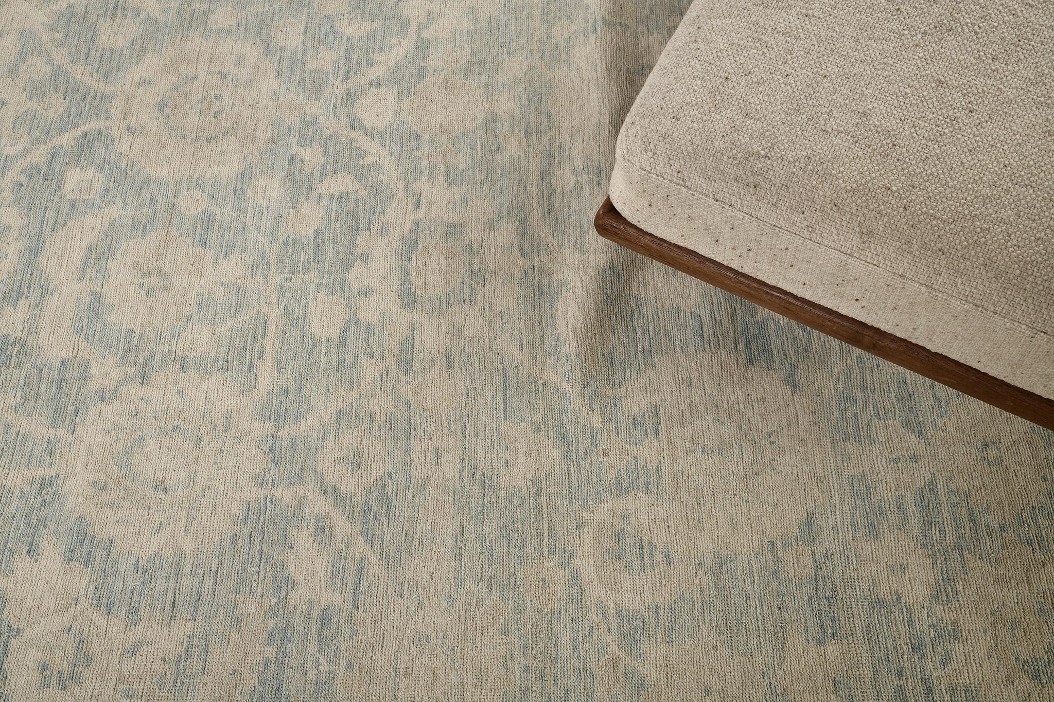 Questo elegante tappeto revival di Trabiz presenta un motivo a specchio di eleganti volute floreali e motivi a forma di vite in color cammello e marrone e un ambiente sommesso di un sottile blu cannella polveroso con motivi simmetrici di confine. 