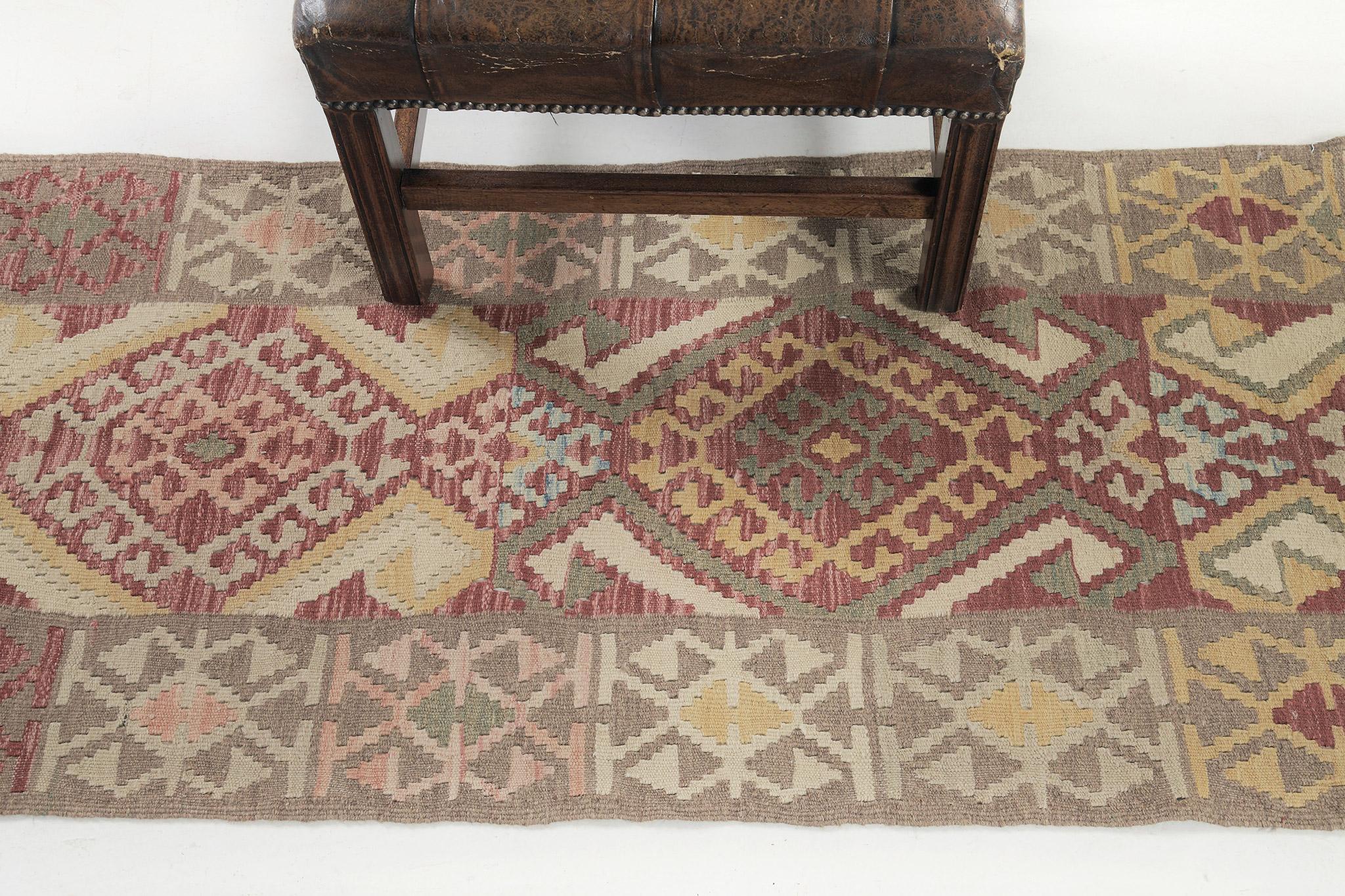 A vintage style flatweave Kilim rug that stars the majestic tones of red, yellow, and khaki. The field is covered with tribal motifs that are composed of wolf's mouths and triangles. The emanating timeless appeal and inimitable warmth are the answer