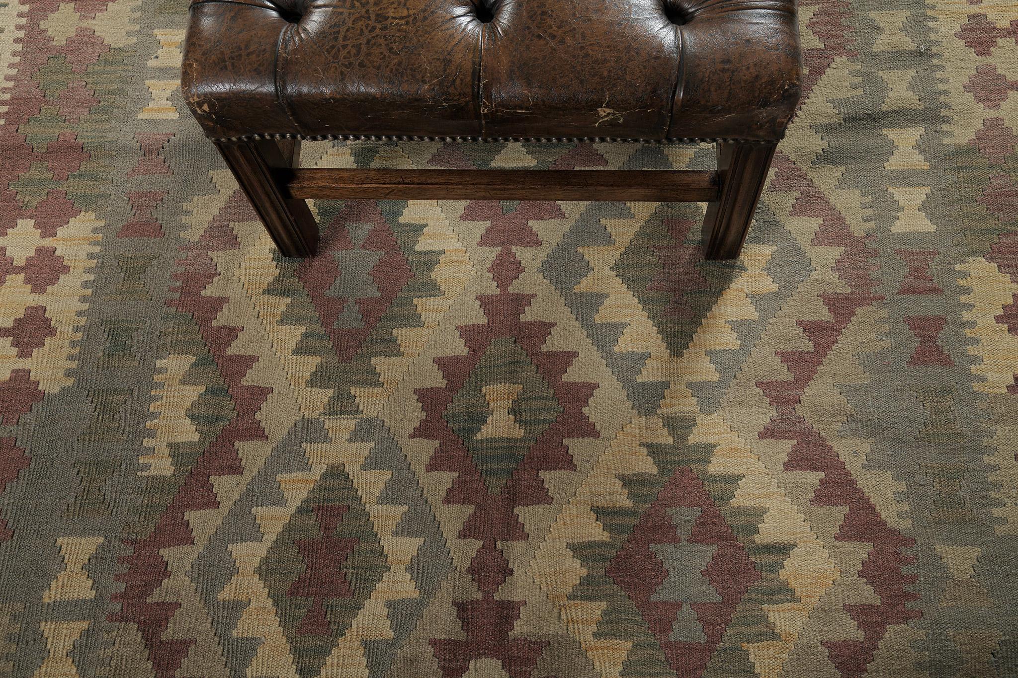 A stylishly remarkable wool vintage-style flat weave Kilim has fantastically flexed its series of the band along the border of zigzag features. It is adorned by tribal motifs of earth tones. The natural color scheme is perfect for a traditional or