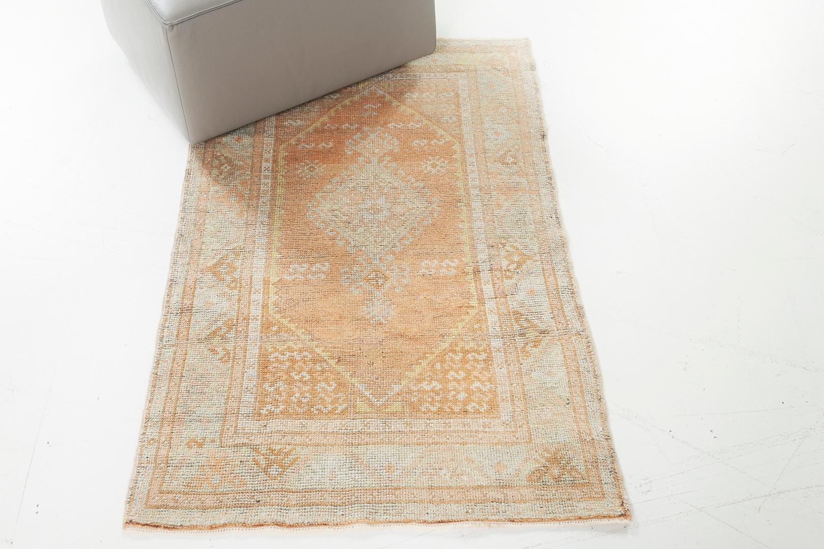 Questo tappeto vintage turco anatolico presenta un maestoso medaglione centrale a losanghe che si staglia su un campo color albicocca. Un bordo a meandro botanico stilizzato, affiancato da bande di protezione floreali interne ed esterne, crea una