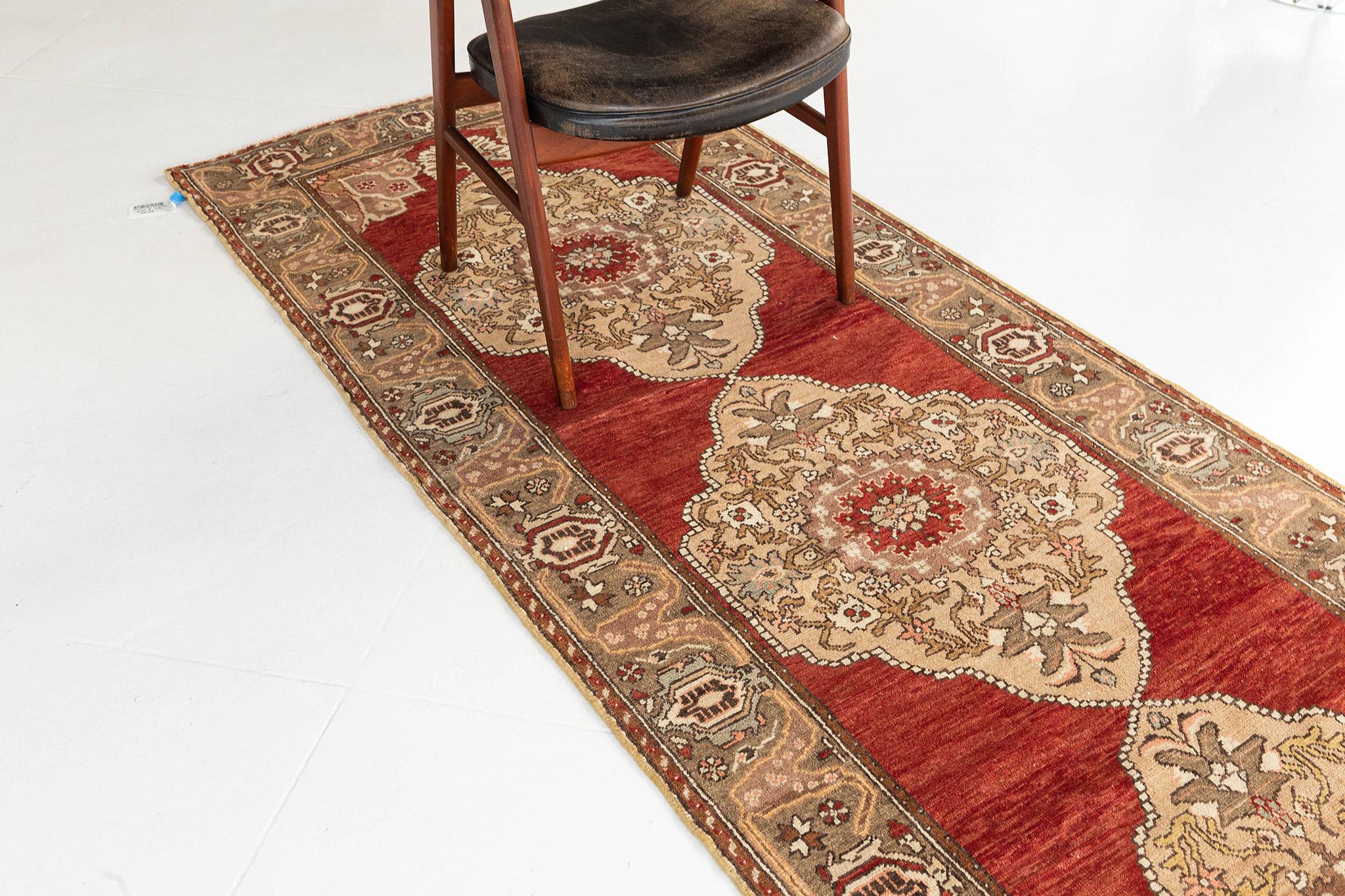 A Vintage Turkish Anatolian runner that features a scalloped diamond-shaped medallions with palmette pendants floating in the center of an abrashed teracotta field. Delicate florid elements adorn the medallion and corner spandrels with a lovely