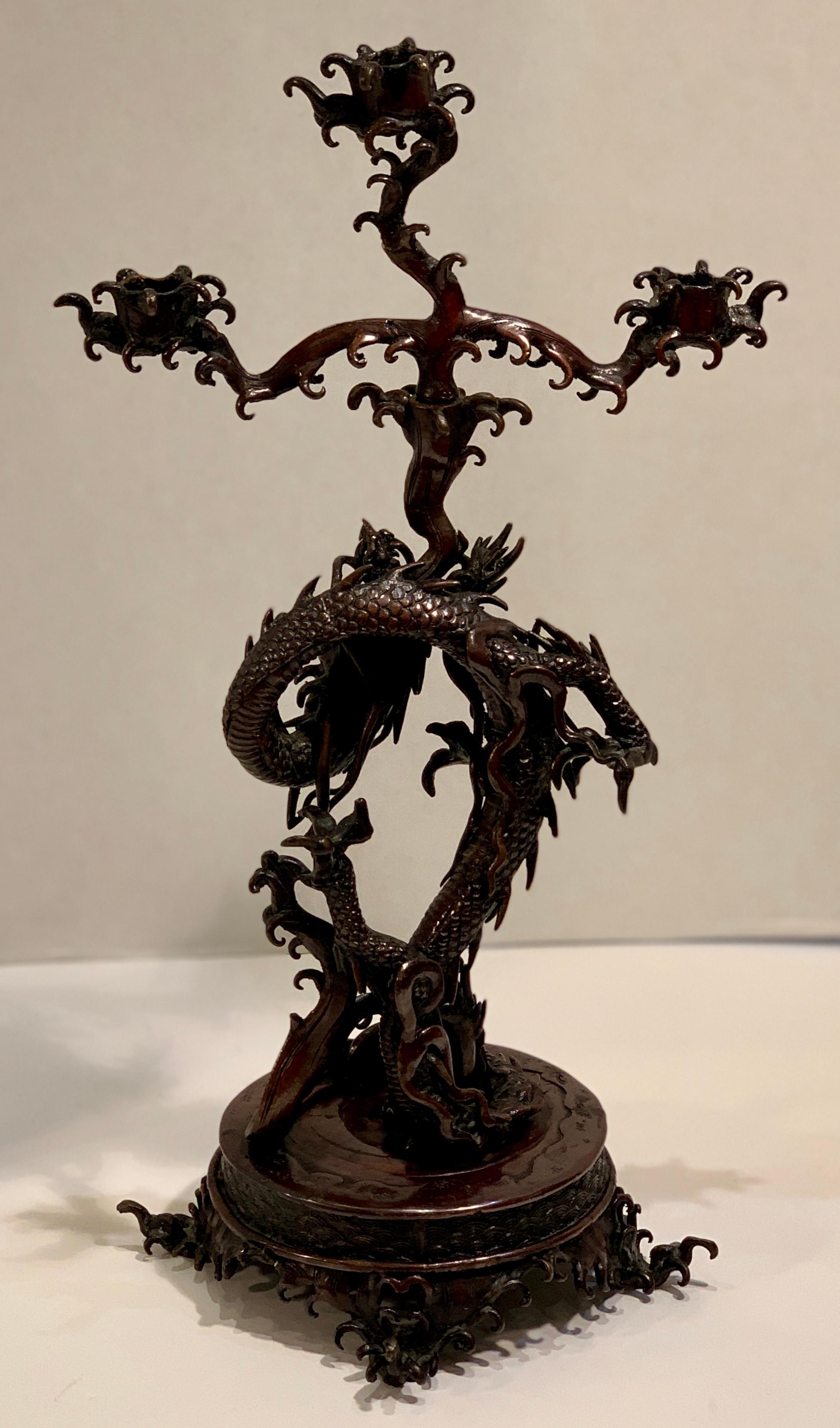 Magnificent and powerful, fantastically sculptural, ferocious bronze Japanese writhing sea dragon candleholder is coiled around itself, with an uplifted head and a stylized plume of water spouting from the dragon’s mouth, which forms the base for