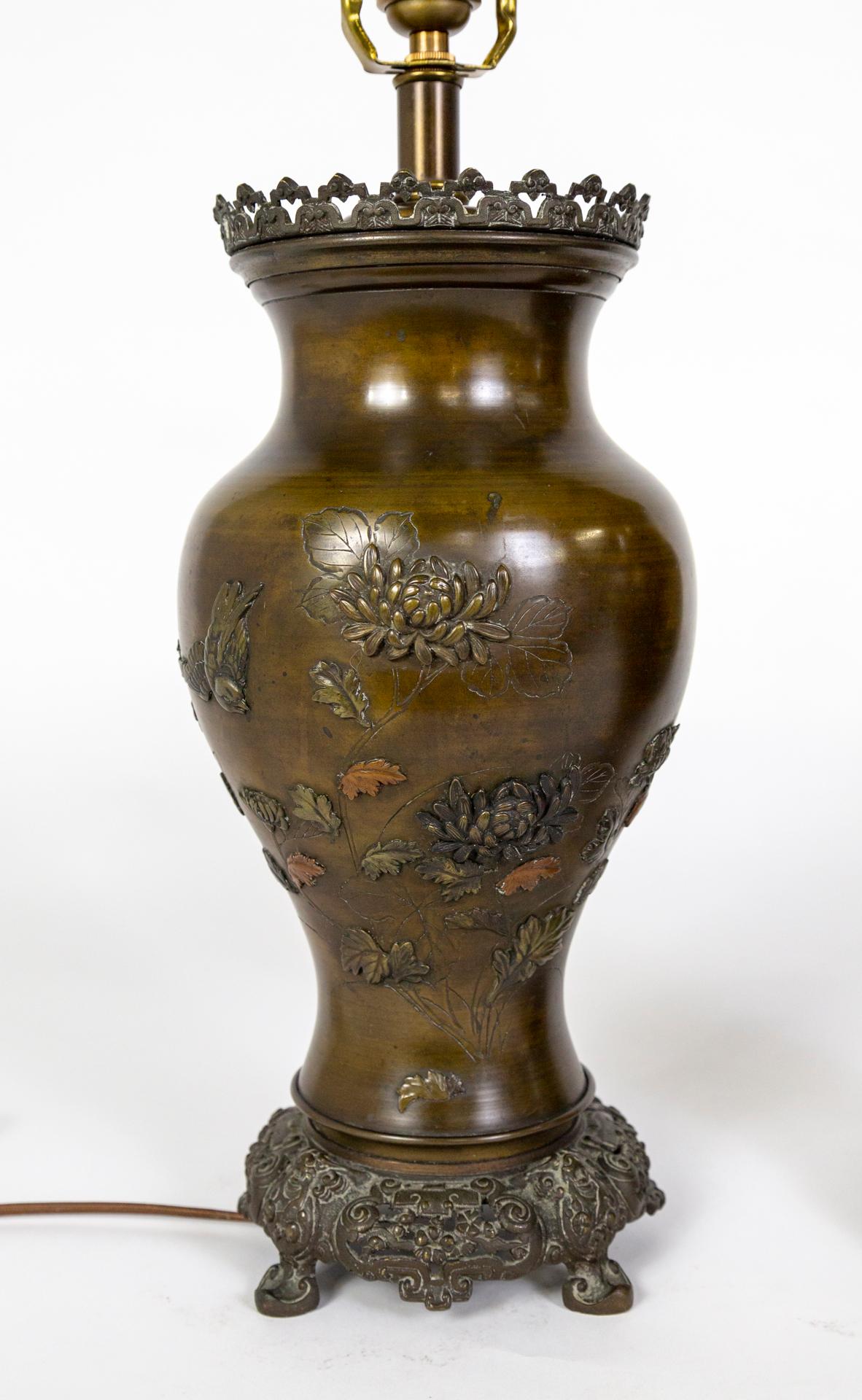 A pair of large, cast bronze, urn-shaped lamps made circa 1885-1890, during the Meiji period (1868-1912) in Japan. They are decorated in both relief and applique with chrysanthemums, birds, leaves, and carved branches. Some of the applied details