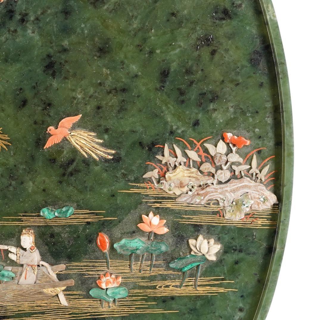 Our large, antique circular jade exhibition screen from the Tsuda family is decorated with abalone shell, malachite, coral, lapis lazuli, pearl, and other hardstones.  Depicted is a lakeside with figures in boats, colorful blooming flowers in the