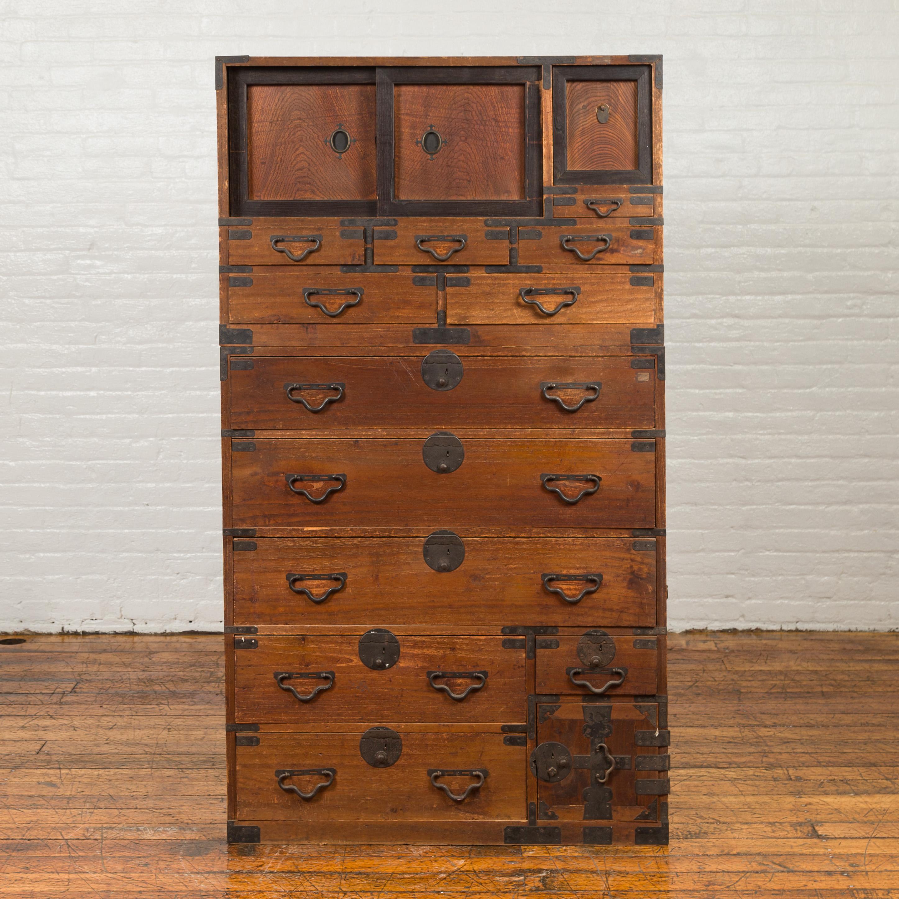 A Japanese Meiji period tall tansu chest from the late 19th century, with drawers and sliding panels. Born in Japan during the later years of the 19th century, this two-section tall tansu chest features two sliding panels and a removable one in its