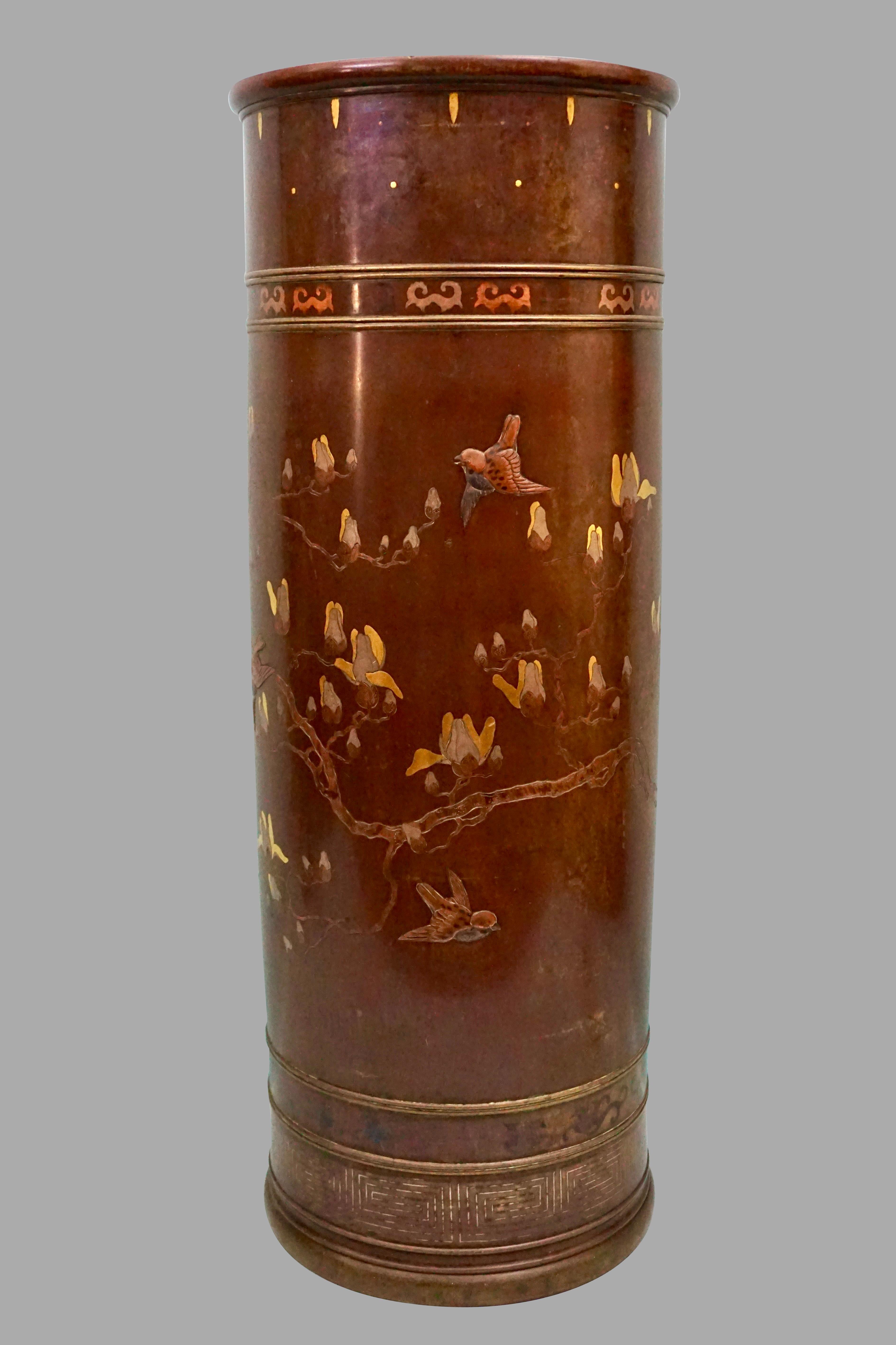 An elegant Japanese Meiji period bronze and yellow metal umbrella holder of cylindrical form, decorated overall with floral and and aviary designs in a garden setting. The small birds and chrysanthemums are executed in relief and form a lovely