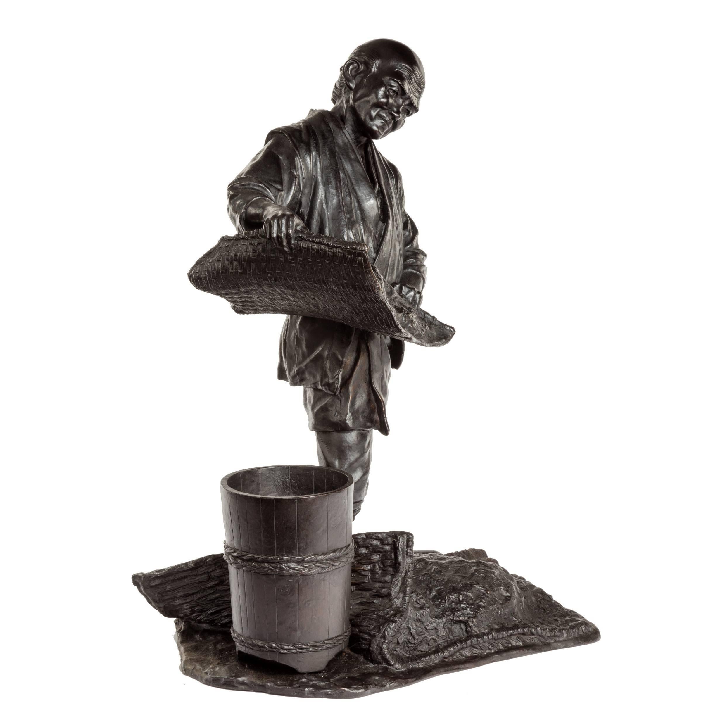 Unusual Meiji period bronze of a labourer sieving through a woven reed mat with another at his feet and a wooden bucket at his side, signed.