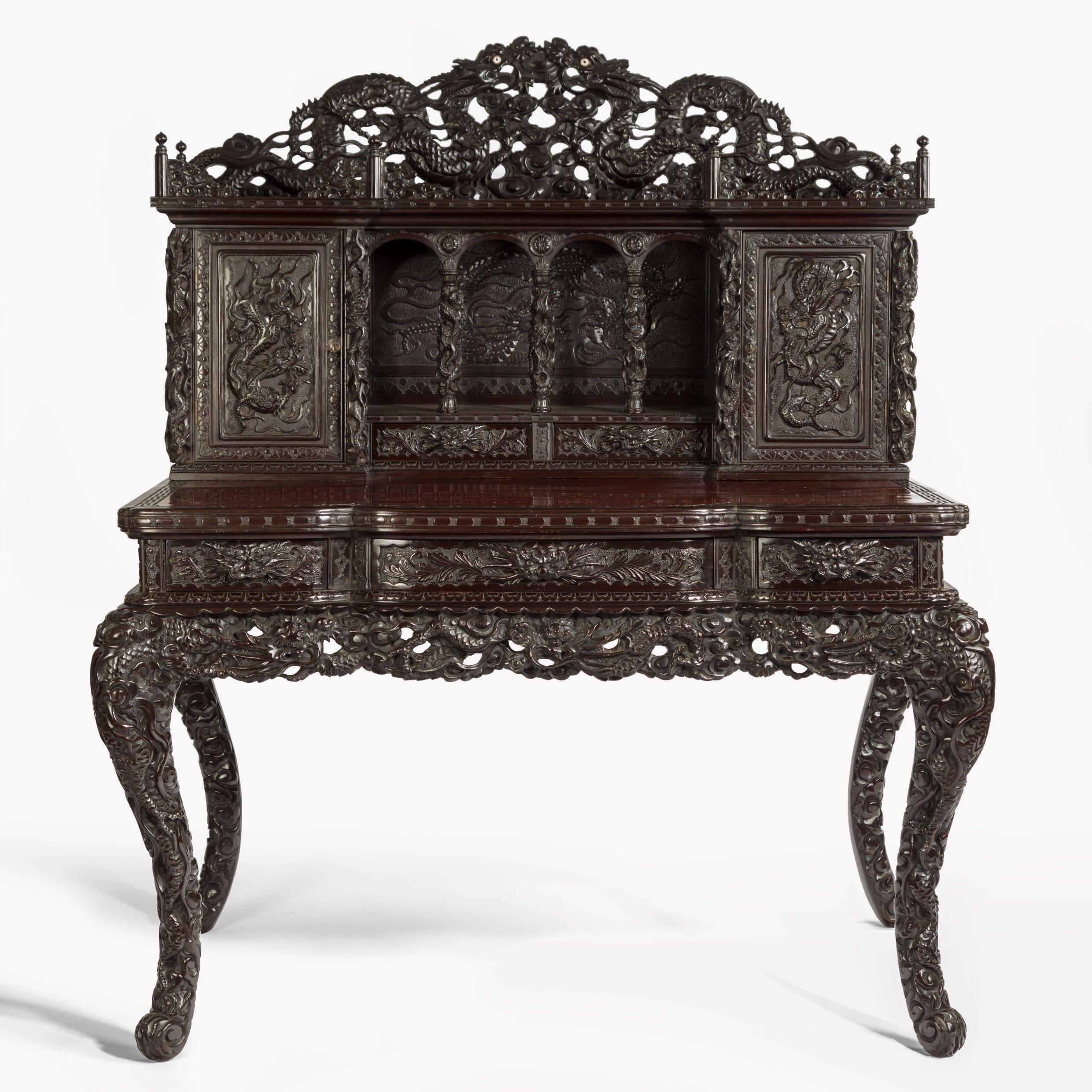 A Meiji period carved hardwood desk and chair made for the Panama California Exposition of 1915-1917, the desk with a shaped rectangular top with two short and one long frieze drawers supported by cabriole legs, the upper section comprising four