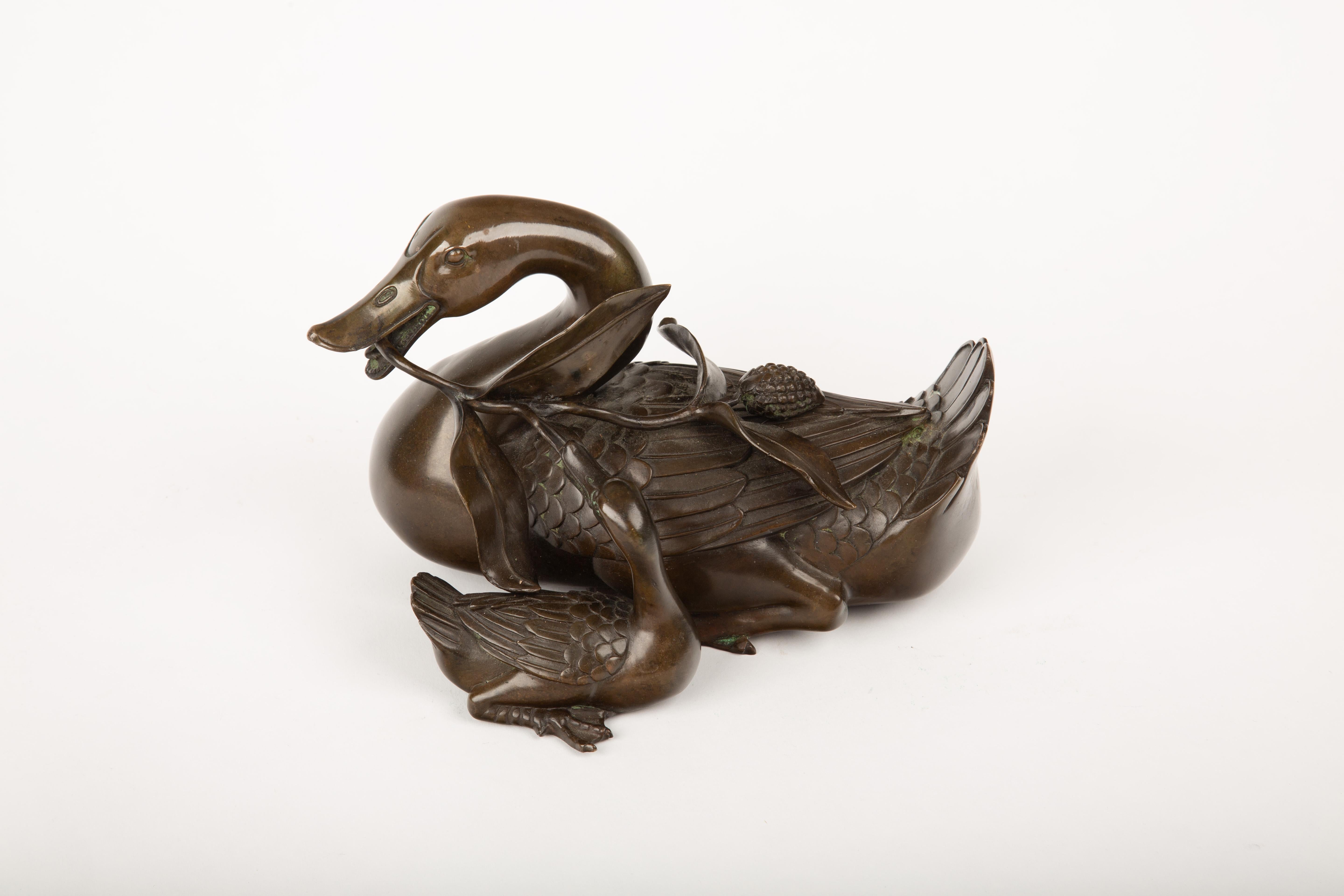 Fein gegossene Bronzeskulptur, die eine Entenmutter mit ihrem Entenküken darstellt, wobei der größere Vogel einen belaubten Lotusstängel im Schnabel hält und eine Lotusschote auf seinem Rücken ruht. Mit außergewöhnlicher Detailgenauigkeit
