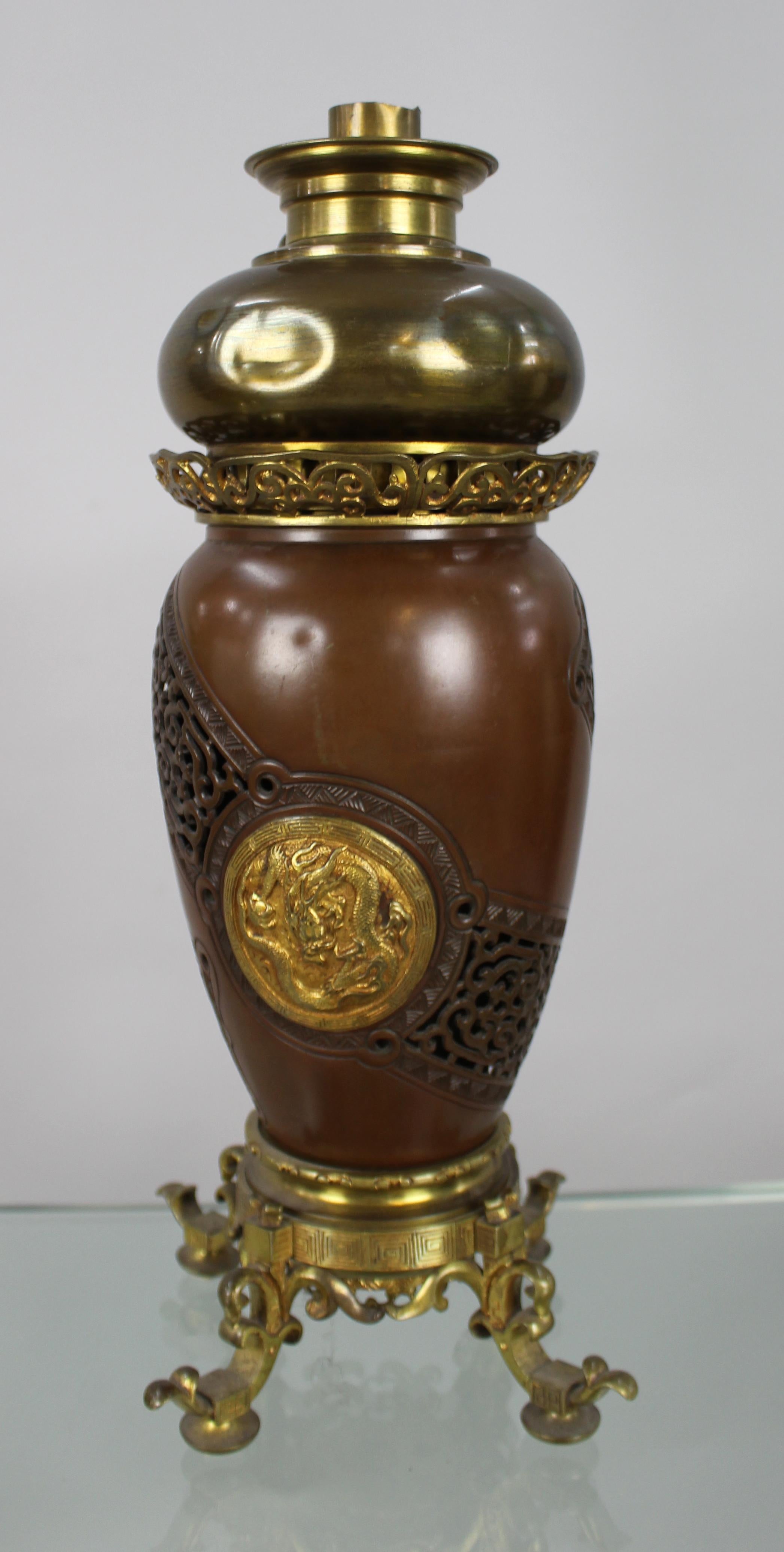 Lampe à huile en bronze d'exportation japonaise de la fin du XIXe siècle ou du début du XXe siècle, de style chinois, qui a conservé son brûleur belge A.W. d'origine. Le corps est en bronze patiné, avec des panneaux ajourés et des rondeaux dorés