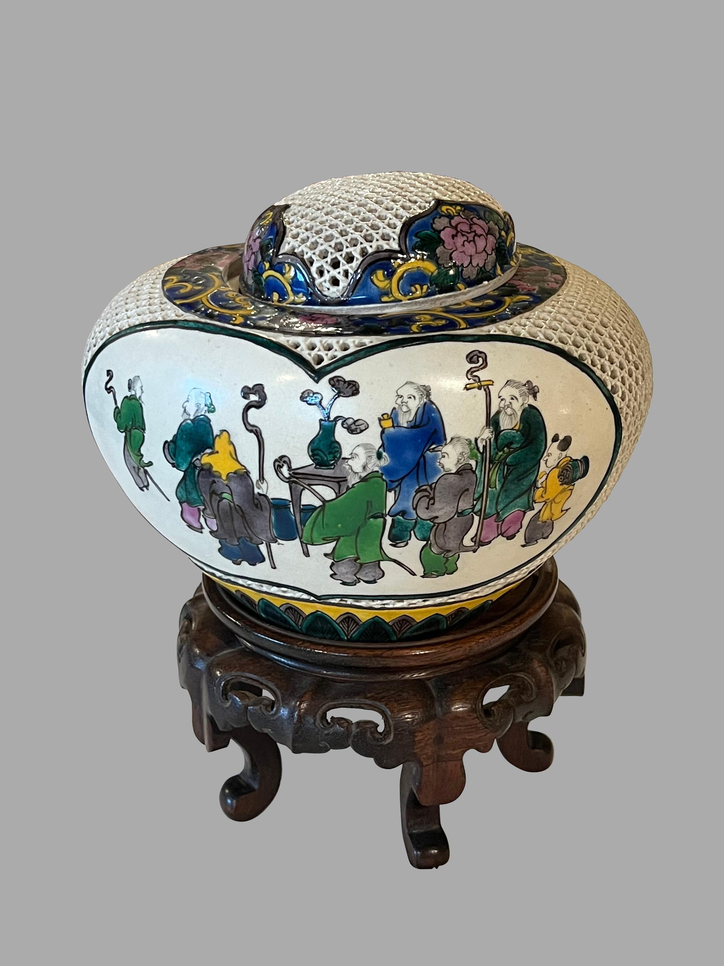 An unusual Japanese Meiji period lidded incense burner or censer with reticulated ovoid body and cap, decorated with a cream background and traditionally garbed people in tones of ochre, green, blue and brown. The landscape depicts trees and a house