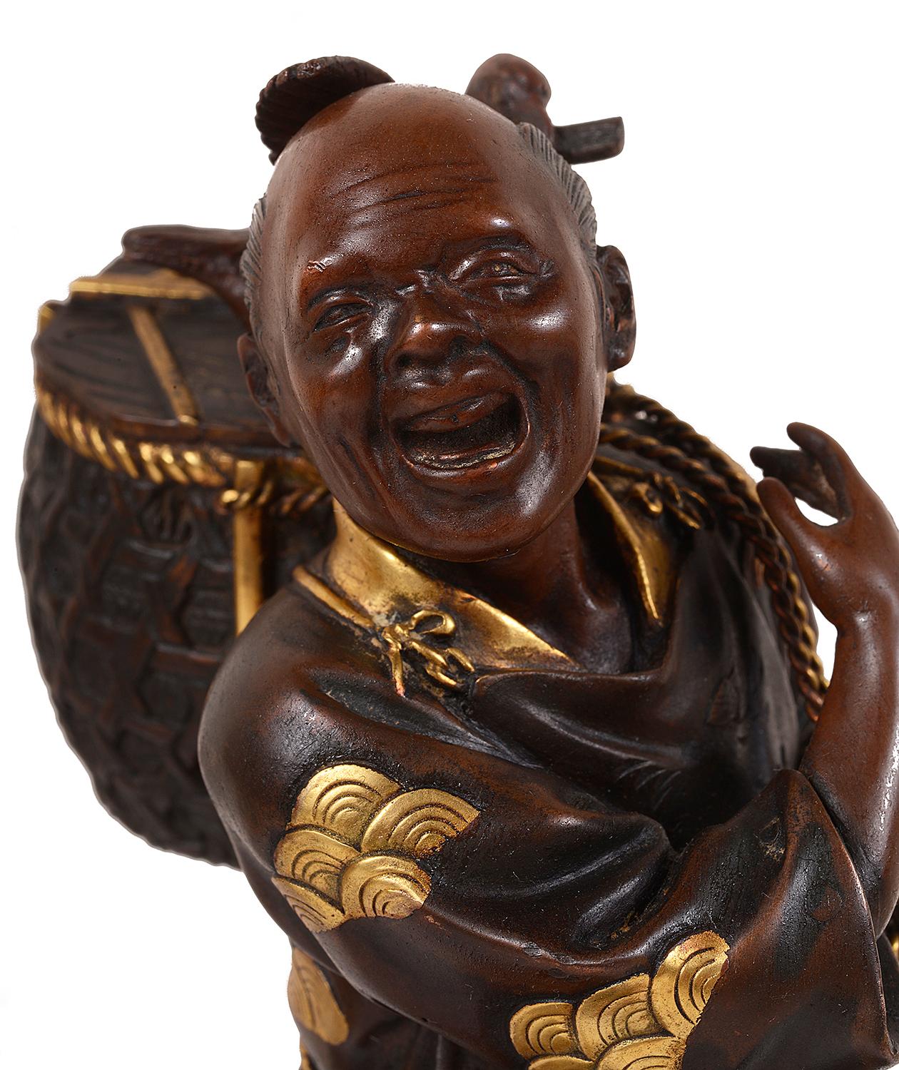A fine quality late 19th century Meiji period (1868-1912) Miayo patinated bronze statue of a bird catch carrying a basket on his back, with gilded highlights, mounted on a carved hardwood base also with gilded decoration.