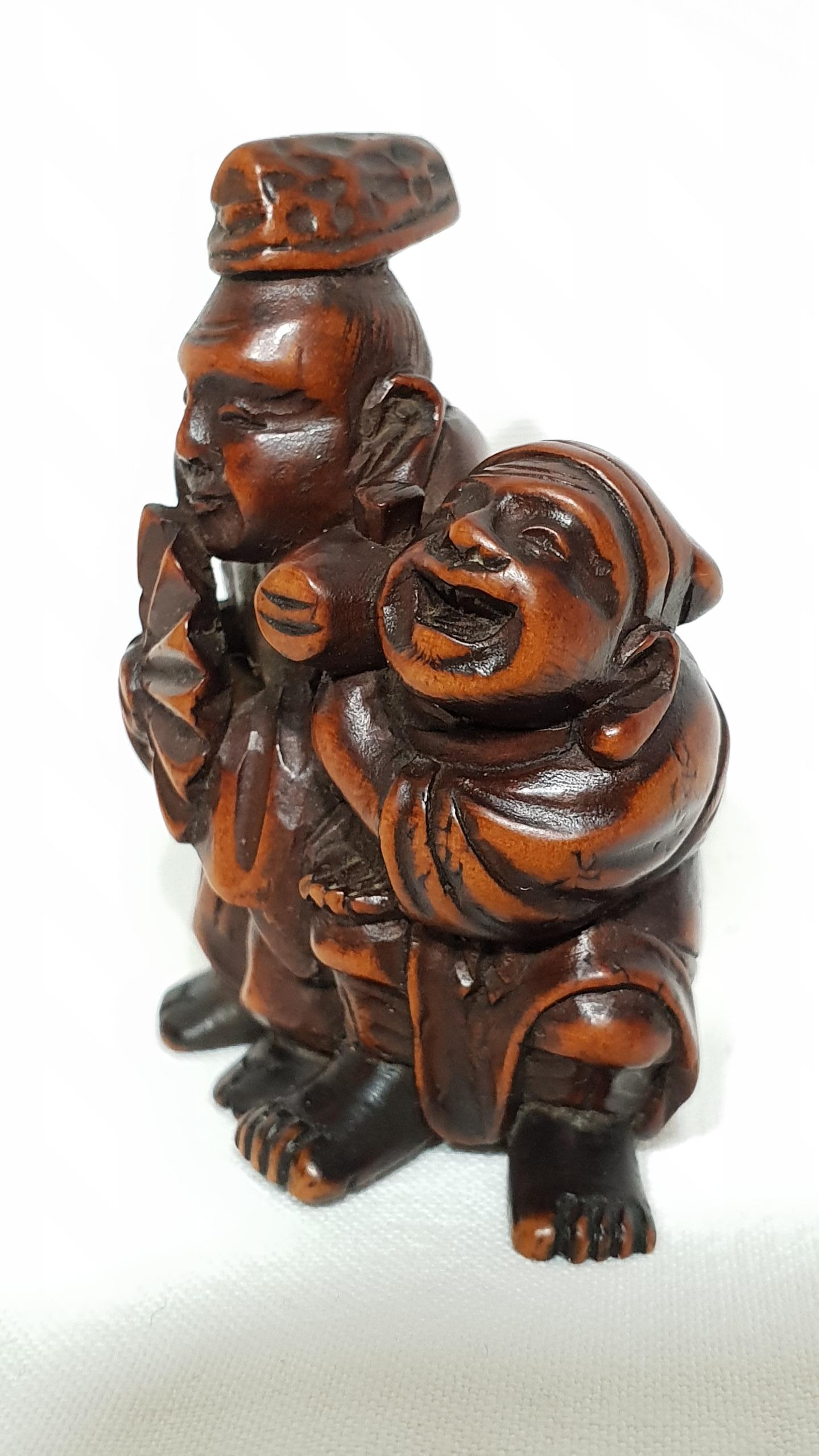 A Meiji period wood netsuke representing street artists dressed as benten and daikoku with Hammer and fan.