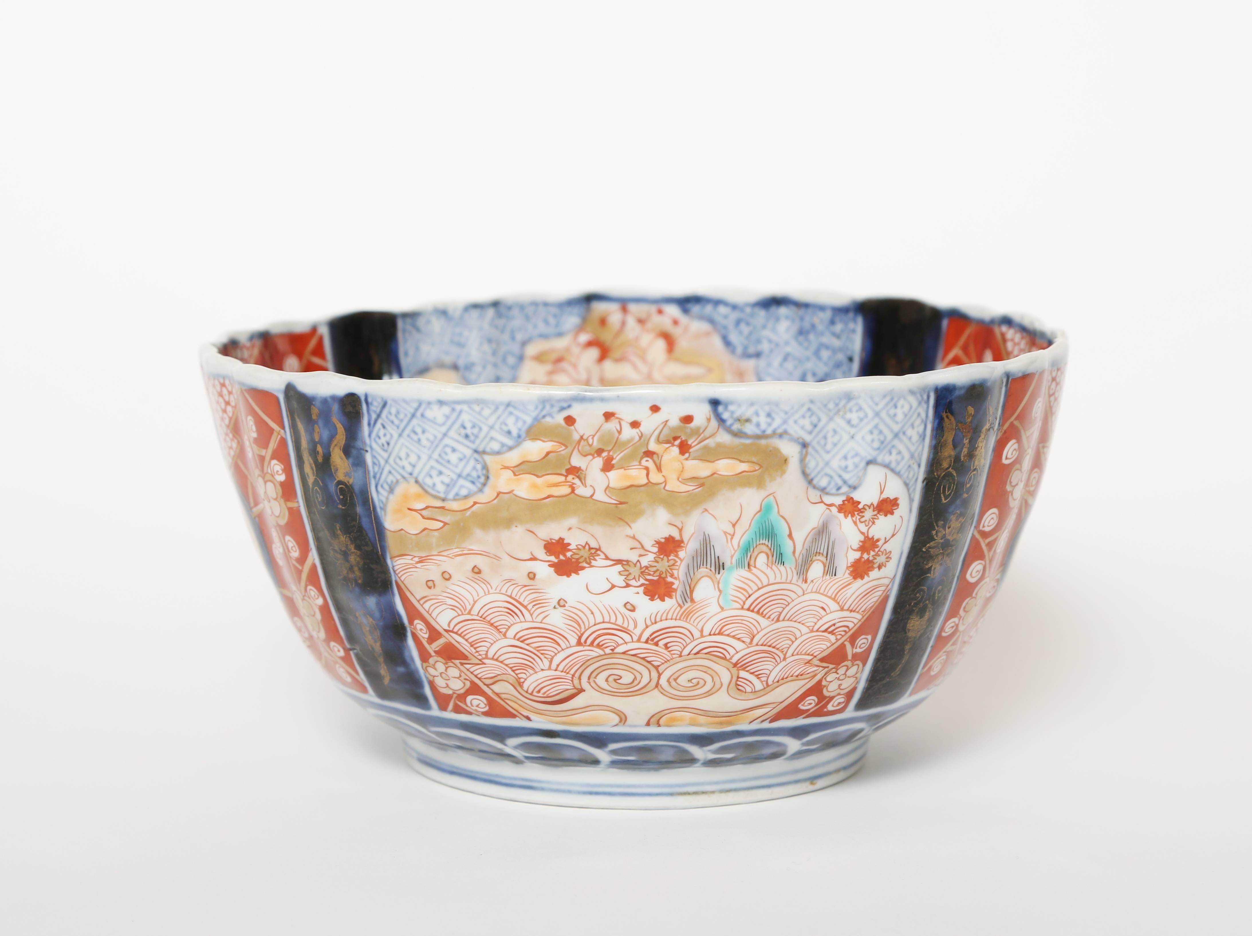 Meiji period scalloped edge Imari bowl. The interior is hand decorated with four panels separated by dark blue bands. The exterior also has four panels separated by dark blue bands. The blue is done in an underglaze method while the iron red,