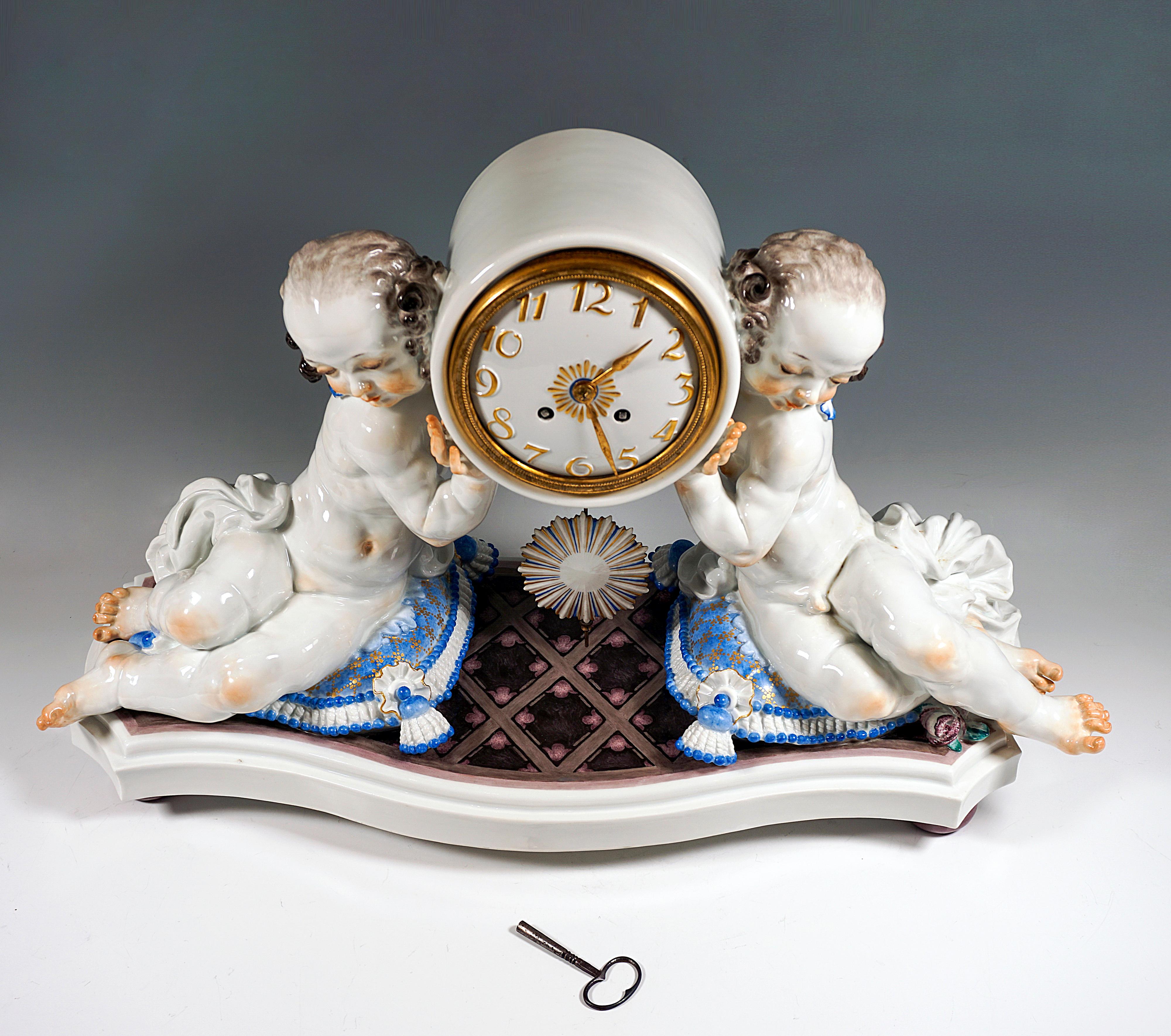 Excellent Meissen Rococo Style Piece of Art:
On a curved base plate with diamond pattern in marble look, sculptured cushions with tassel decoration, on the side seated figures, girl and boy, who gracefully carry the round clock case. White porcelain