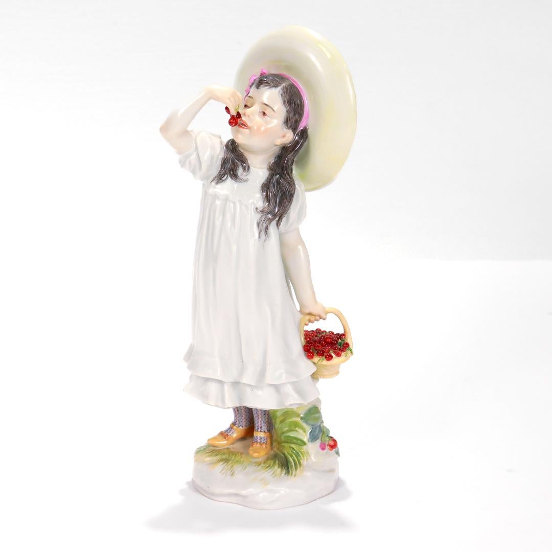 A fine German Art Nouveau porcelain figurine.

By Meissen.

Modeled by Paul Helmig.

Depicting a a girl holding a basket of cherries in one hand and eating cherries with the other. Dressed in a white dress, polychrome socks, yellow shoes and a large