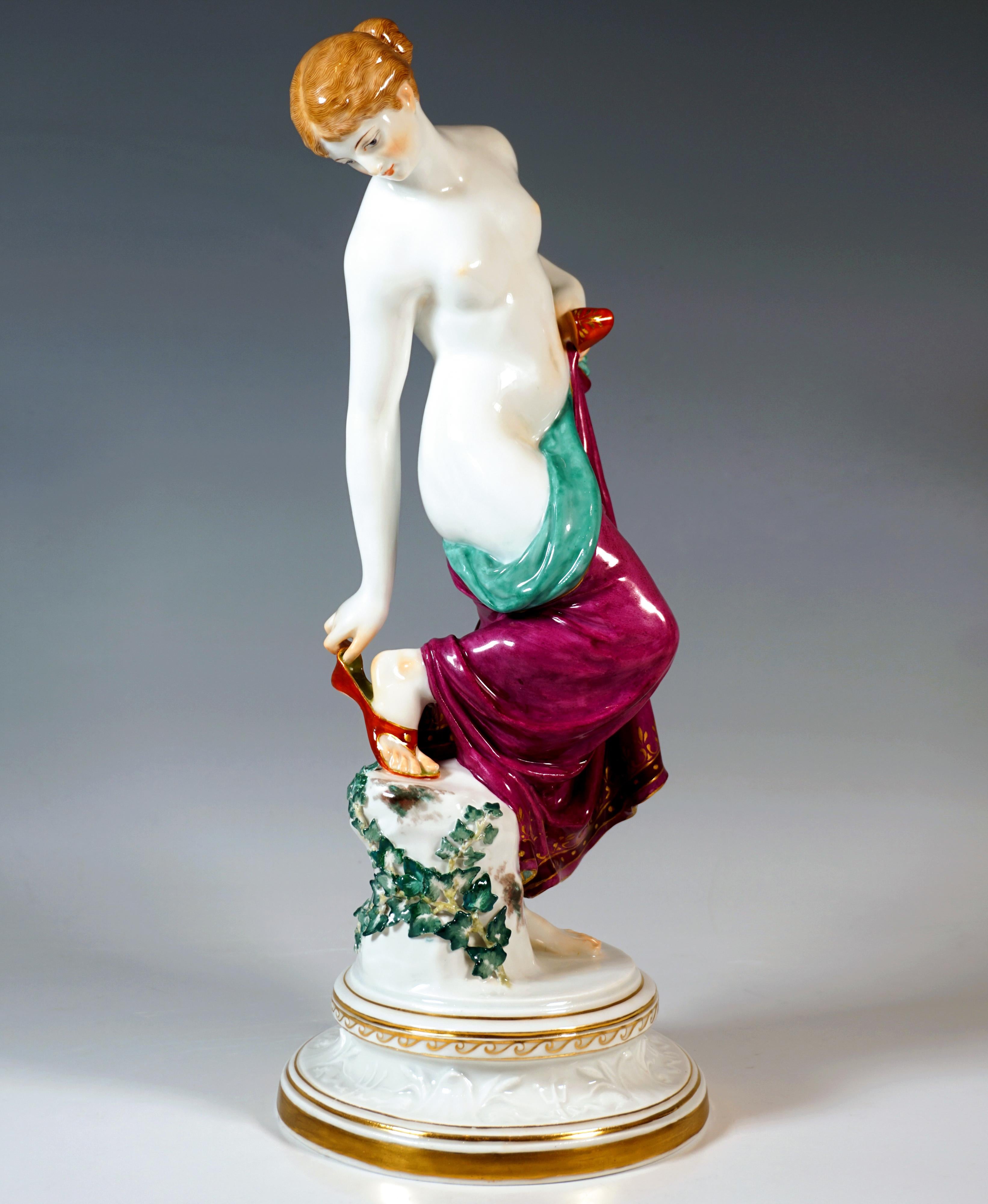 Extremely decorative, fully sculpted representation of a naked young beauty with her hair tied back, covering her nakedness after her bath with a softly draped cloth, which she holds with one hand at her left hip together with a 
bathing shoe, while