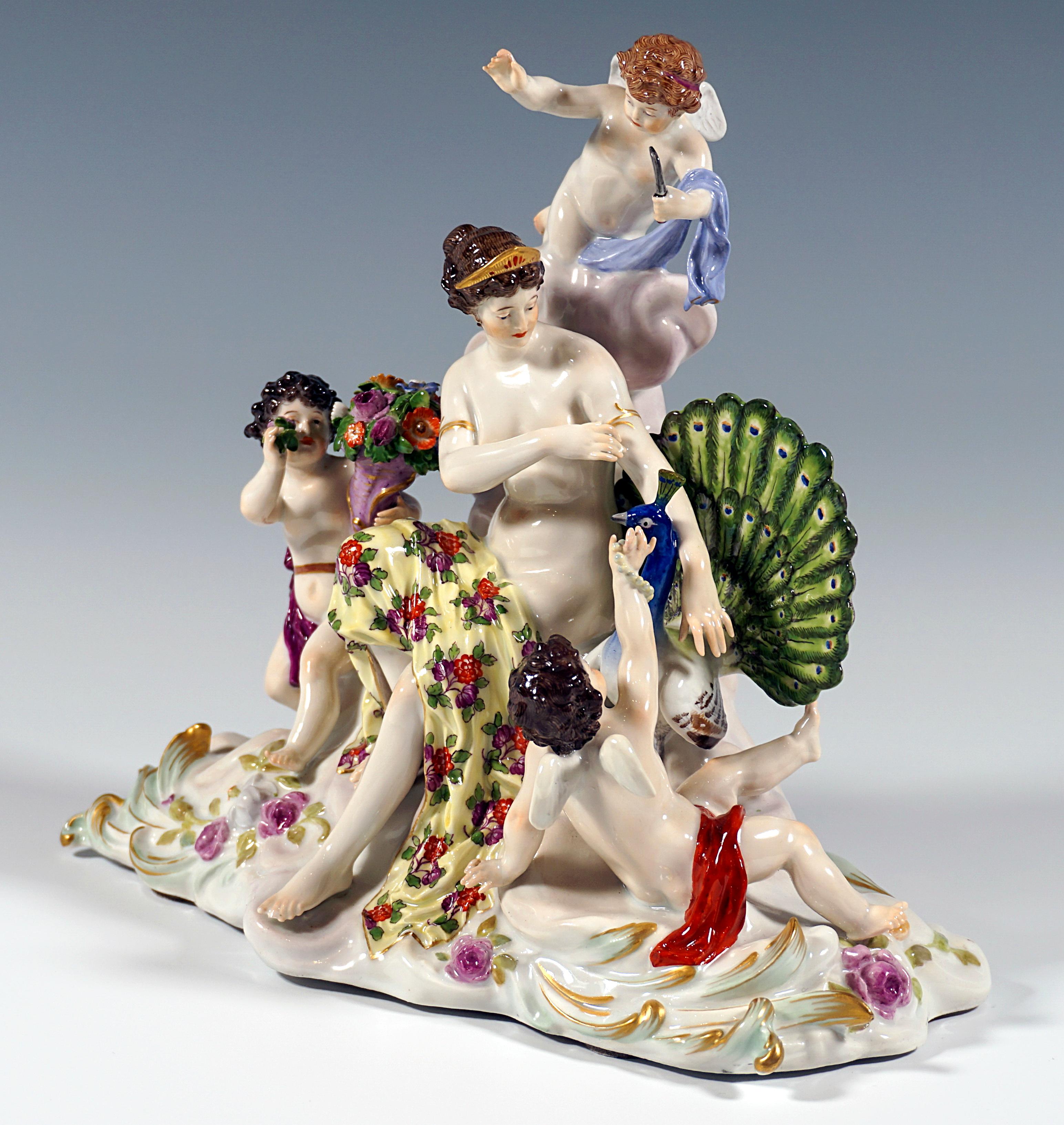 Very rare and excellent Meissen porcelain group around 1900:
Juno, the Roman goddess of the air (Greek Hera), as a young woman with her hair pinned up, covered only with a cloth, sitting on a cloud, adorning herself with bracelets, next to her