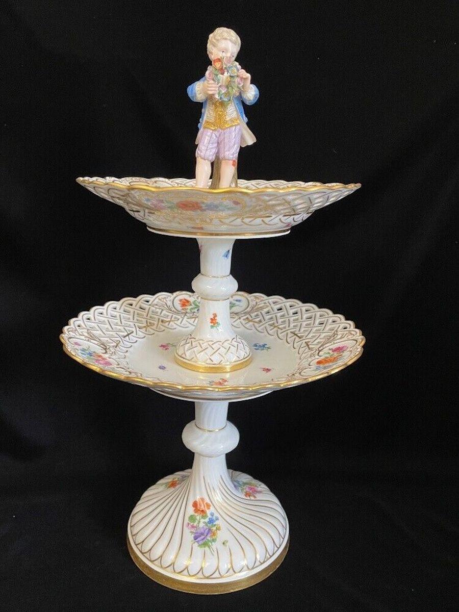 Table centerpiece with two levels and a lovely figurine of a young boy on top. 
Nicely painted with some rich gilding. Very nice condition. The upper level is 20 cm in diameter, the lower one 24 cm. Each part individually marked.