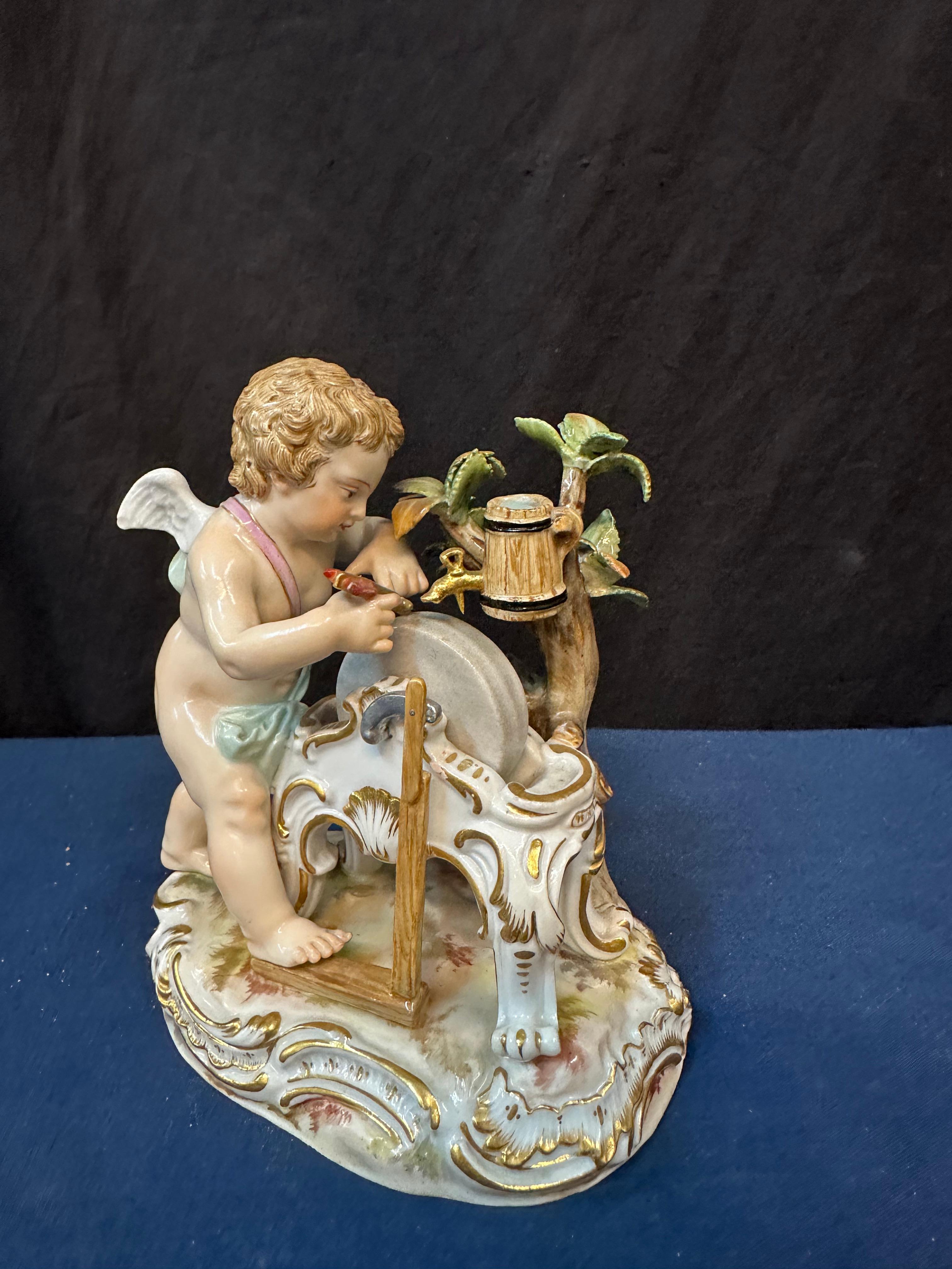 This vintage Meissen curio cabinet porcelain dates from the late 19th century. The charming beautifully hand painted sculpted cherub is working his grinding wheel sharpening love arrows. The soft, though vivid, hand coloration accentuate his face &