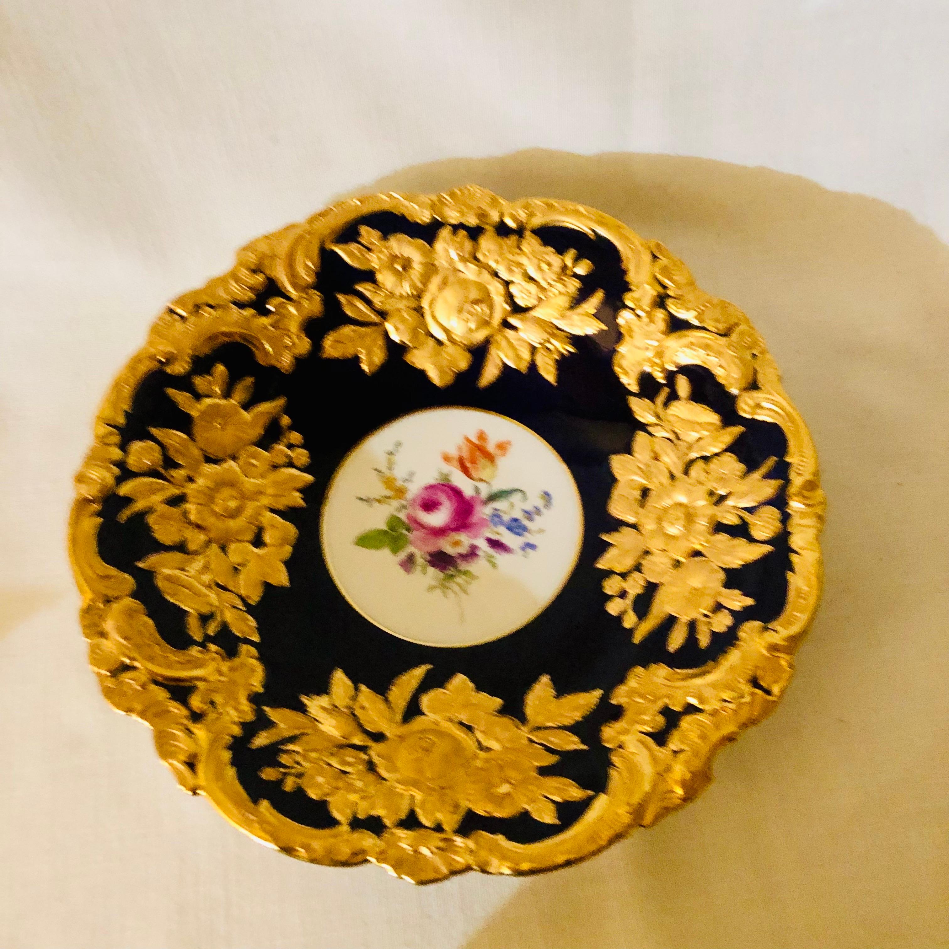 This is a stunning cobalt Meissen Charger. It is decorated with raised gilded flowers and leaves. Its fluted border also has heavy gold. It has a central hand-painted bouquet of flowers. It is really a beautiful eye-catching charger, with all its