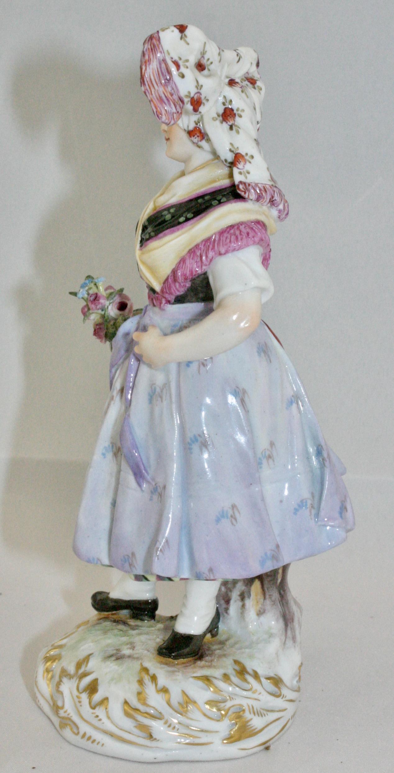 Meissen figure of Lusatian woman holding flowers in national costume, circa 1887. This model designed by Hugo Speiler. It is marked with the Meissen mark, model number Q190d, '52,' and '44' on the base. The figure is 6 inches tall X 2 7/8 inches