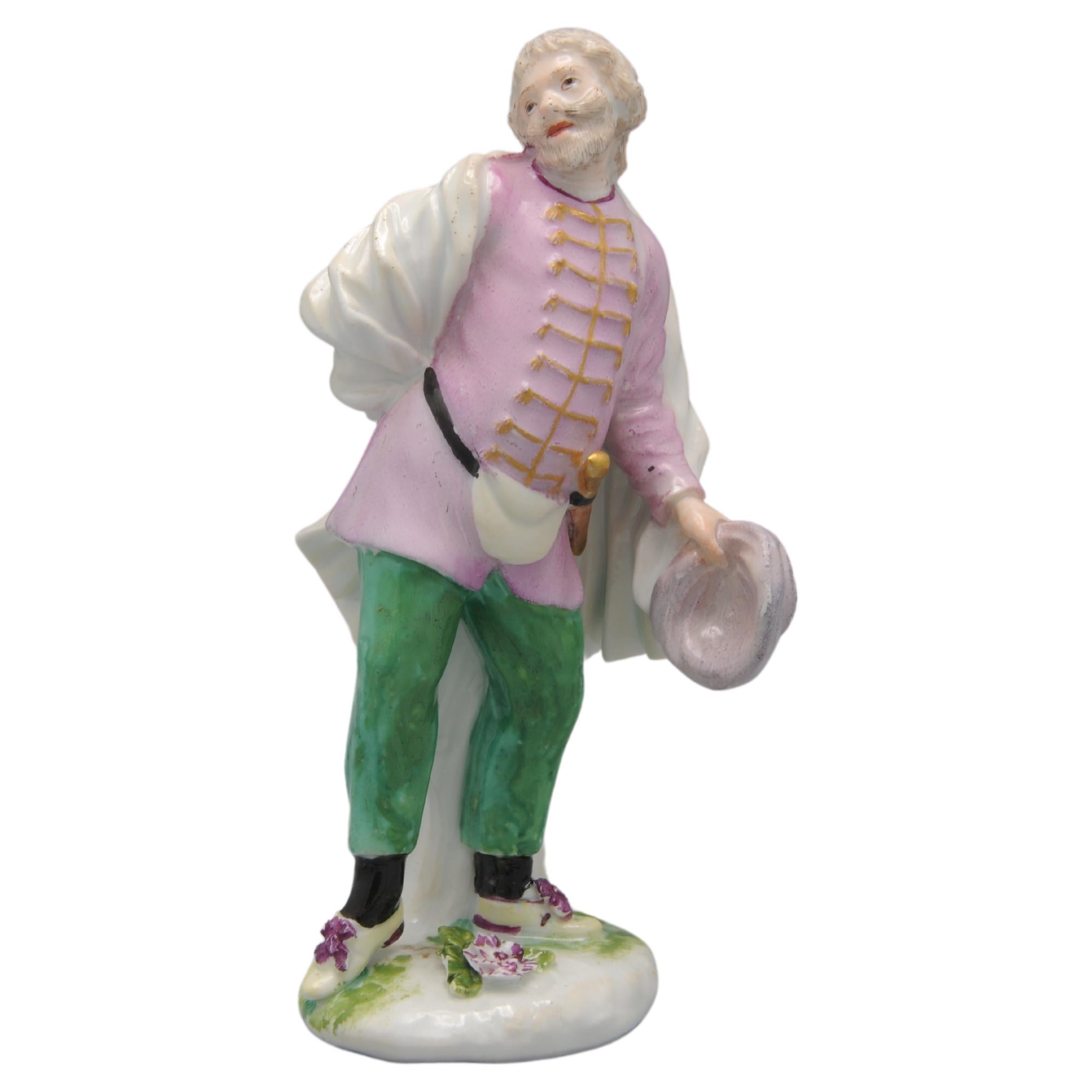 Modelo Meissen de commedia dell'arte de Scapino por Peter Reinicke, c. 1744.
En pose danzante, con un sombrero amarillo en la mano izquierda y un cinturón con daga dorada y monedero. Con capa y chaqueta de color rosa con botones dorados sobre