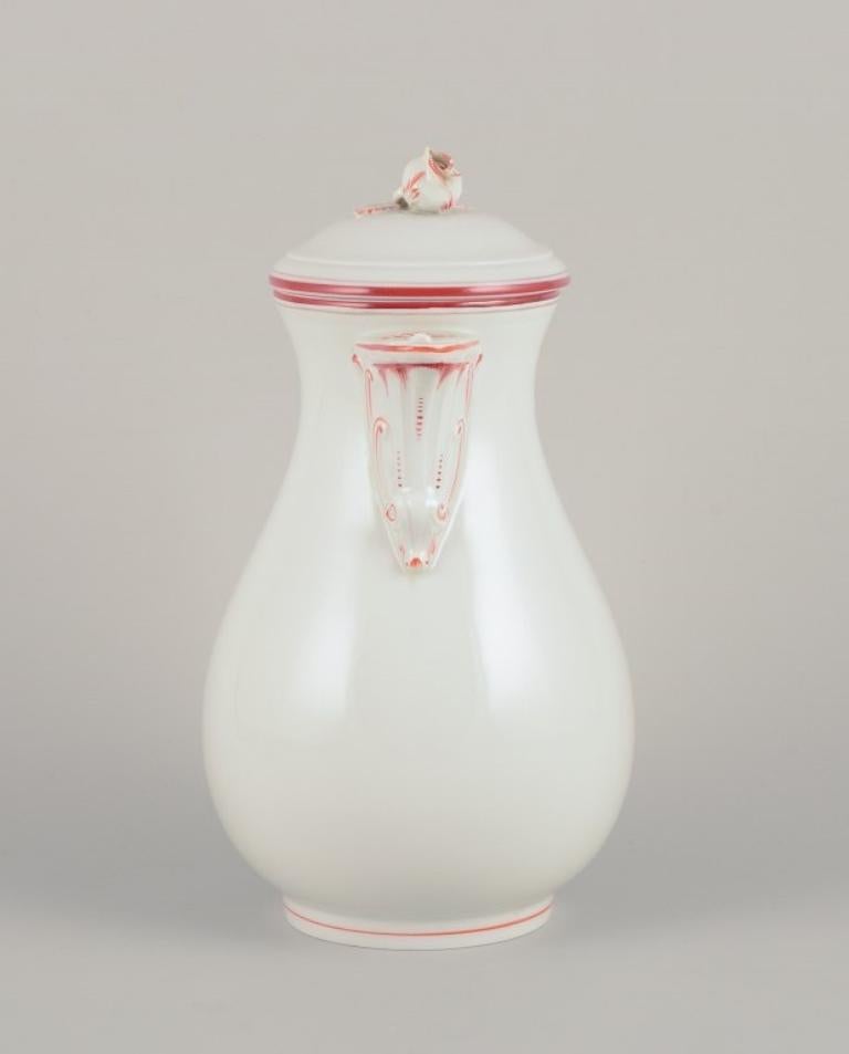 Meissen, Alemania. Cafetera decorada con ribete rojo coral. 
Un pomo de tapa con forma de rosa.
Aproximadamente en la década de 1930.
Marcado.
Tercera calidad de fábrica.
En muy buen estado. Tapa con un desconchón en el interior y desconchones