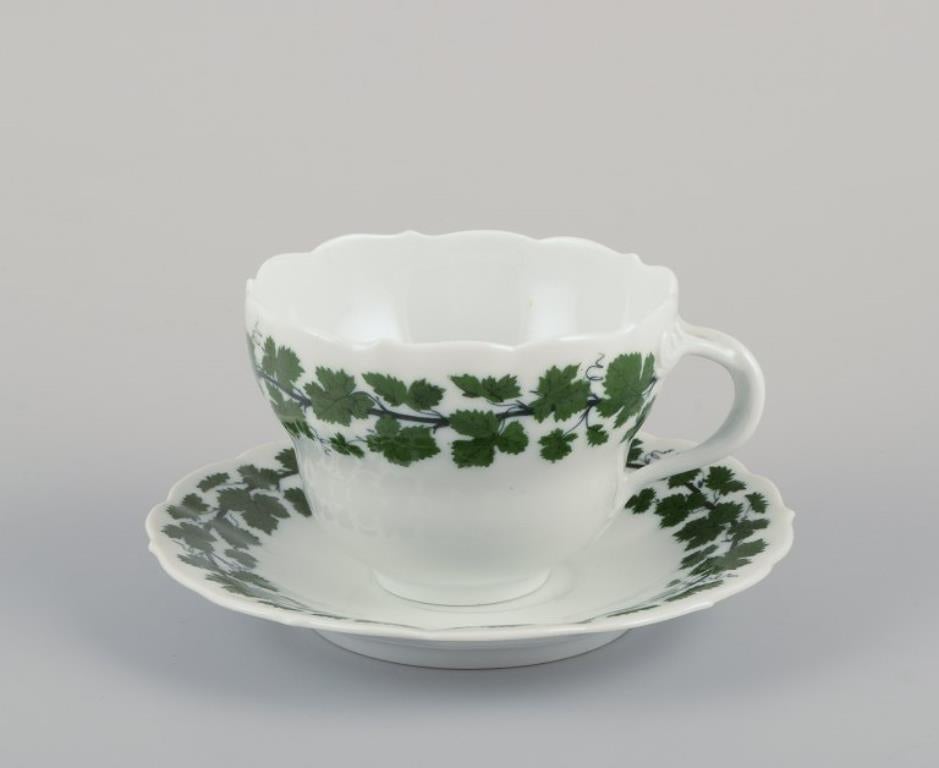 Meissen, Alemania, Vid de hiedra verde, dos grandes tazas de desayuno con platillos. 
Pintado a mano.
Años 20/30.
Marcado.
Una taza es de primera calidad de fábrica. Una taza es la quinta calidad de fábrica.
En perfecto estado.
Taza: H 9,0 - 10,0 cm