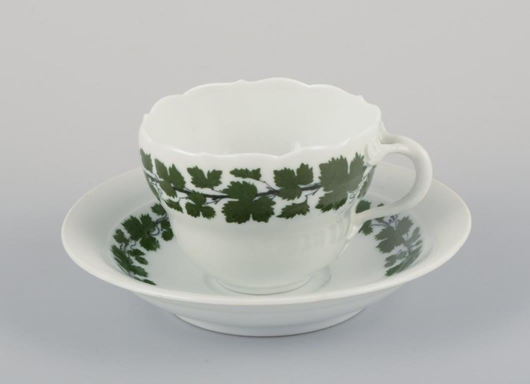 Meissen, Alemania, Vid de hiedra verde, dos tazas grandes de café con platillos a juego. 
Pintado a mano.
Años 20/30.
Marcado.
Tercera calidad de fábrica. Un platillo es de primera calidad de fábrica.
En perfecto estado.
Tazas: P 8,5 cm x A 6,5