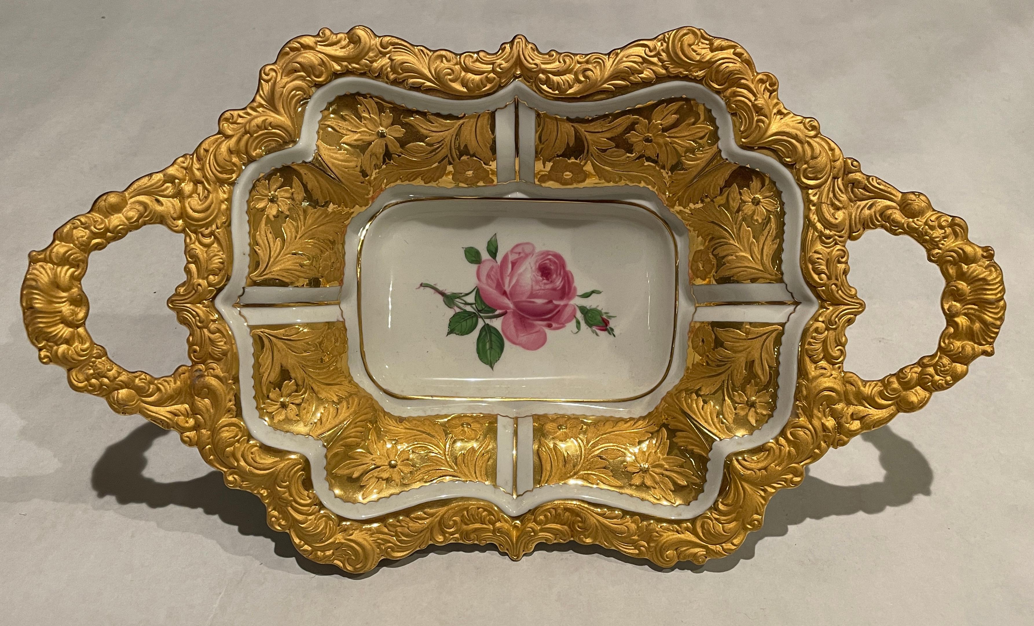 Two handled Meissen heavily gilded charger or tray with pink rose painted flower in center and raised gold flower and leaf decoration on interior panels as well as rim and handles. Crossed swords with top center dot date this beautiful platter to