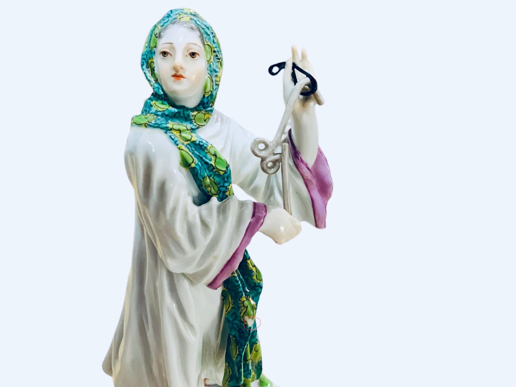 A Meissen Porcelain figurine of a Middle East lady. It depicts a lady dressed with a white and pink robed garb. She is wearing a Middle East headdress painted green and turquoise color. She is standing up over a square porcelain base adorned with