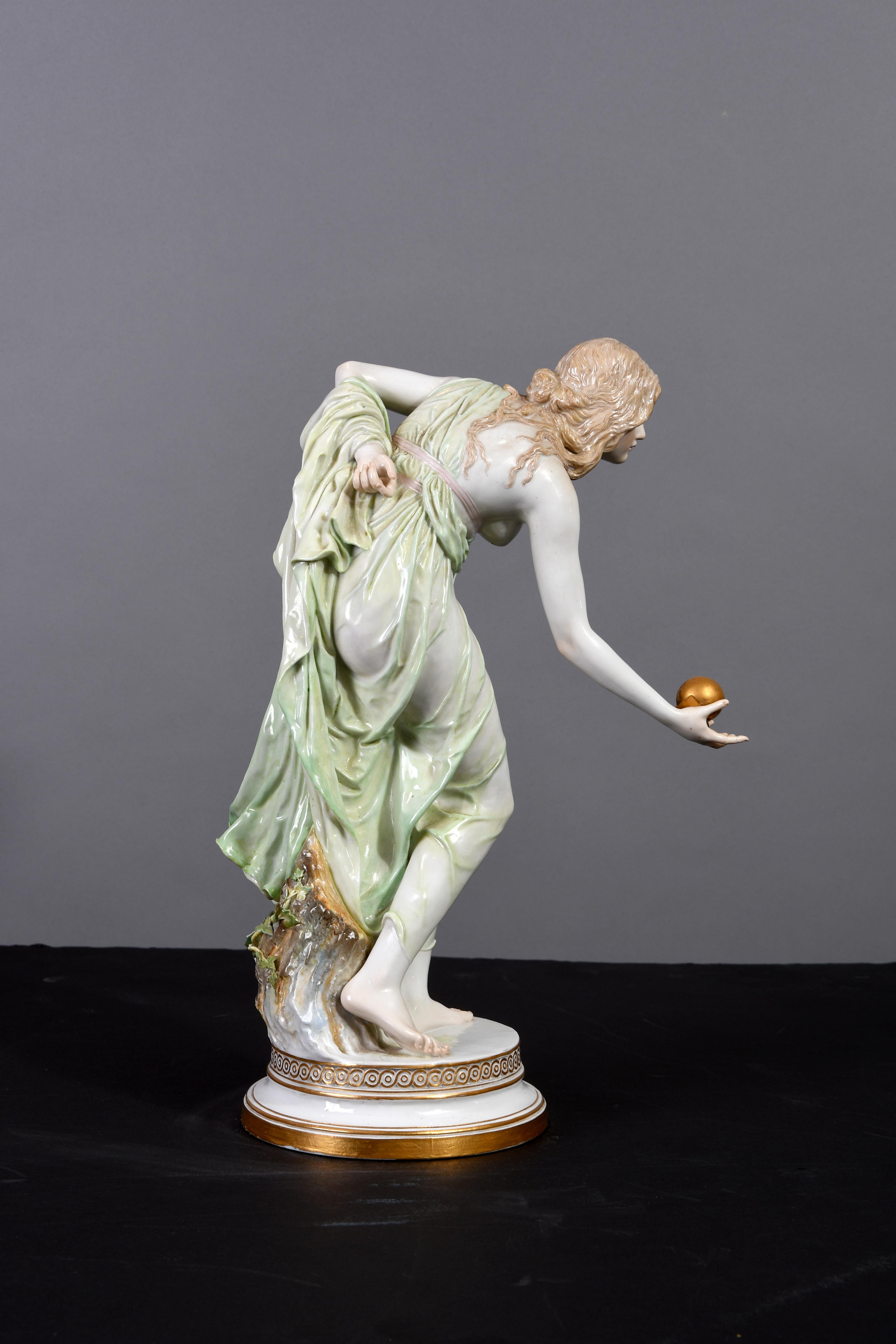 A nymph woman, dressed with a shear light green robe, ready to throw a ball. The porcelain is marked with the Meissen hallmark blue crossed swords below the round base. The ball and the base are painted in gold while the nymph dress is light green.