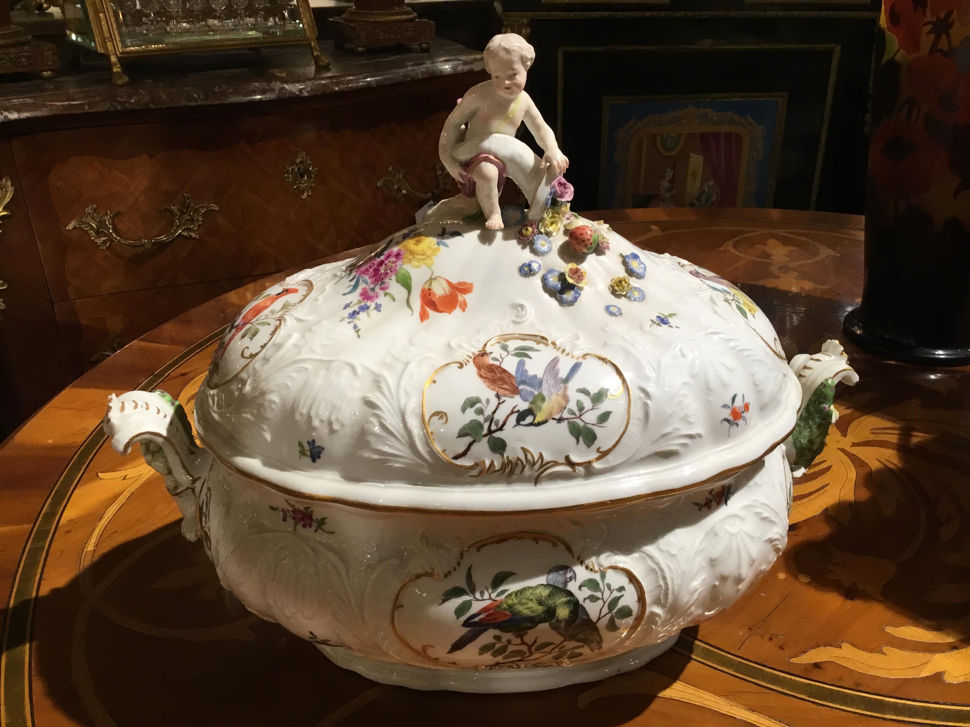 Beautiful and in pristine condition. Very fine quality with a figure of a putto
On the crest holding a cornucopia filled with raised flowers and fruits spilling
Forward on the top of the tureen. Colorful birds are painted in cameos on 
All sides