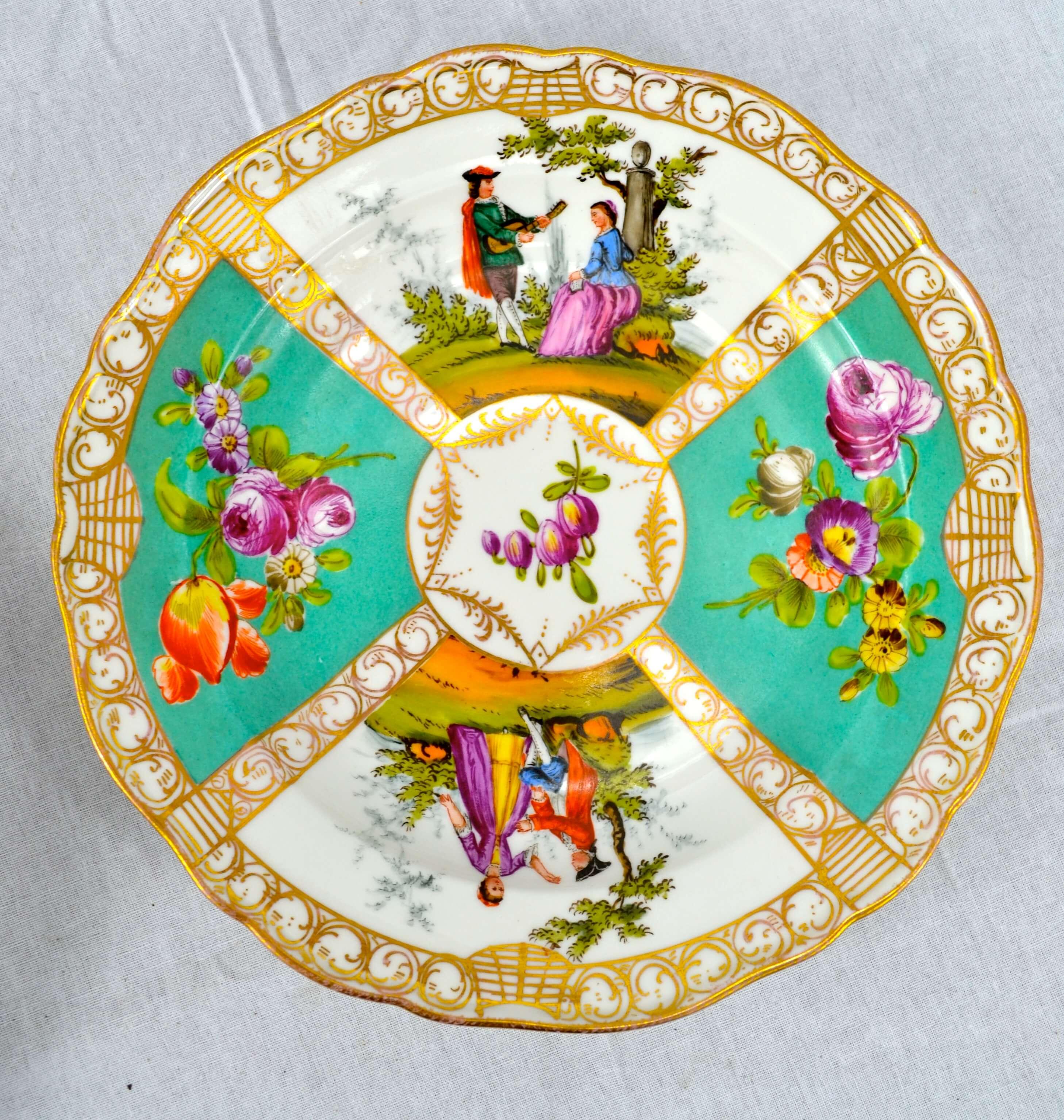 A set of six Meissen plates. Each plate has a different colour palette and shows a different idyllic scene of a couple in a romantic landscape. The two other painted quadrants and the centre depict different types of flowers, all in a gilded border.