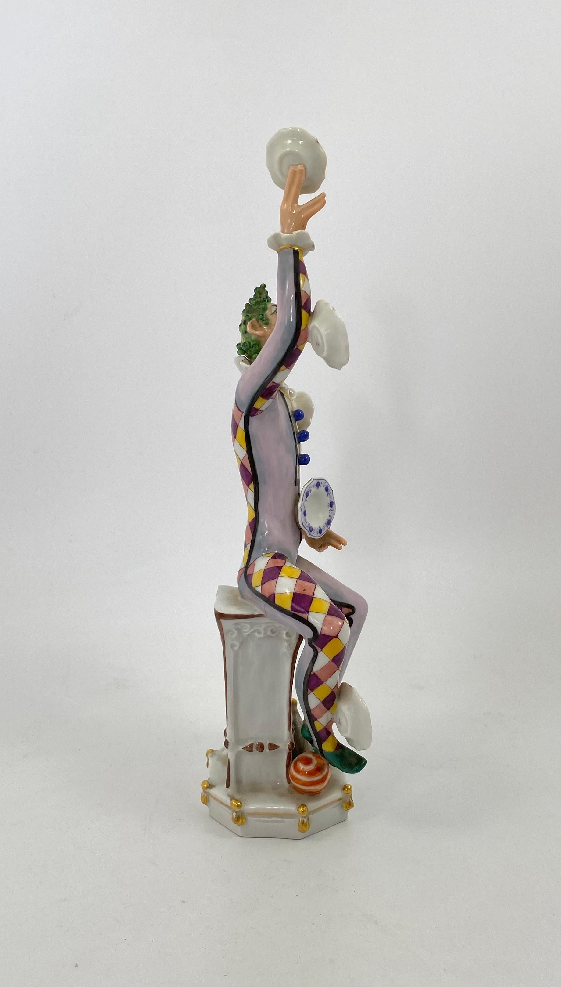 Meissen porcelain figure ‘Der Jongleur’, 1976. This wonderfully conceived figure, modelled by Peter Strang, as a clown juggler, dressed as Harlequin, juggling five Meissen ‘Onion pattern’ plates. He is seated upon an architectural column, sprigged