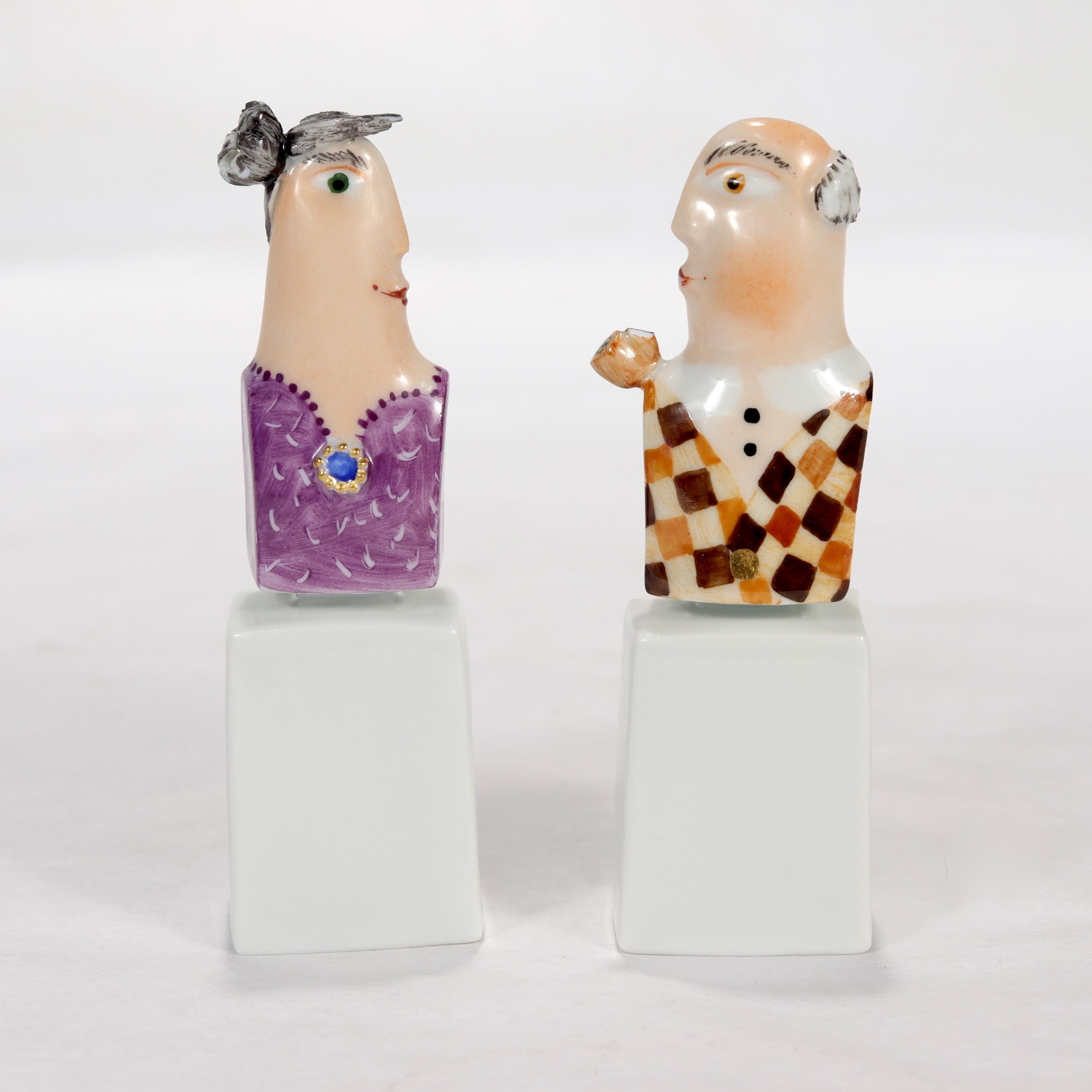 A fine pair of miniature Meissen porcelain busts.

By Peter Strang. 

In the form of a man and woman in casual clothing. The man wears an argyle sweater and is smoking a pipe, and the woman is in a purple dress with a blue brooch.

Each bust rests