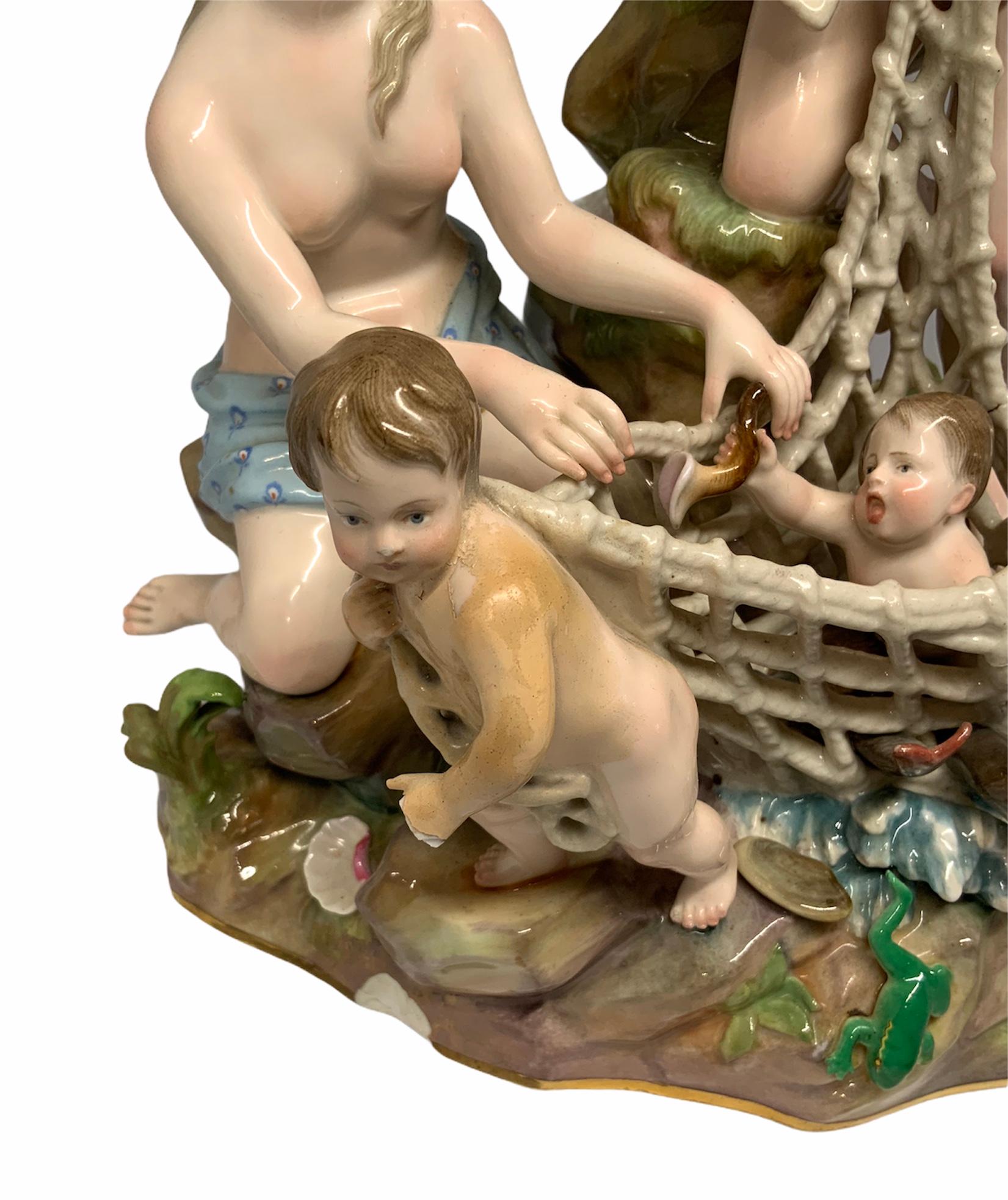 This is a Mythological Meissen group Porcelain figurines depicting two semi nudes nymphs and a nude child holding a fishing net that catches a baby, some fishes and a frog that is escaping from it. They are over a large rock base and some water are