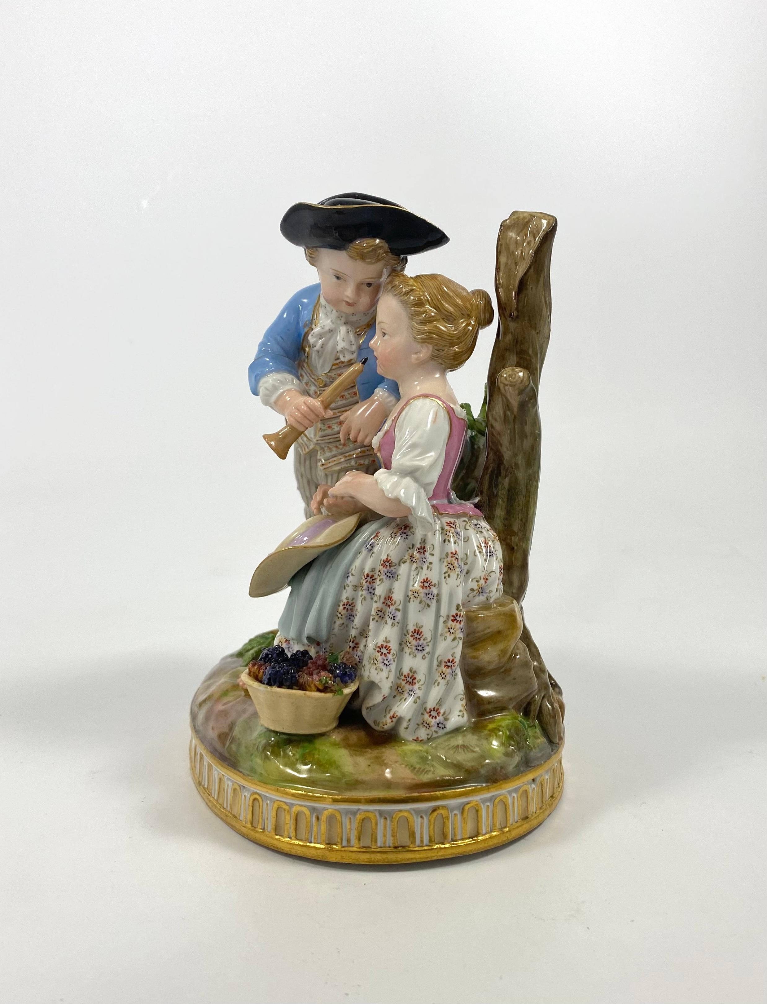 Meissen porcelain figure group, c. 1880. Finely modelled as two children wearing 18th Century costume. The boy offers the girl pipe to play, whilst she seats next to a basket of grapes.
The figure is set upon a grassy mound oval base, edged with
