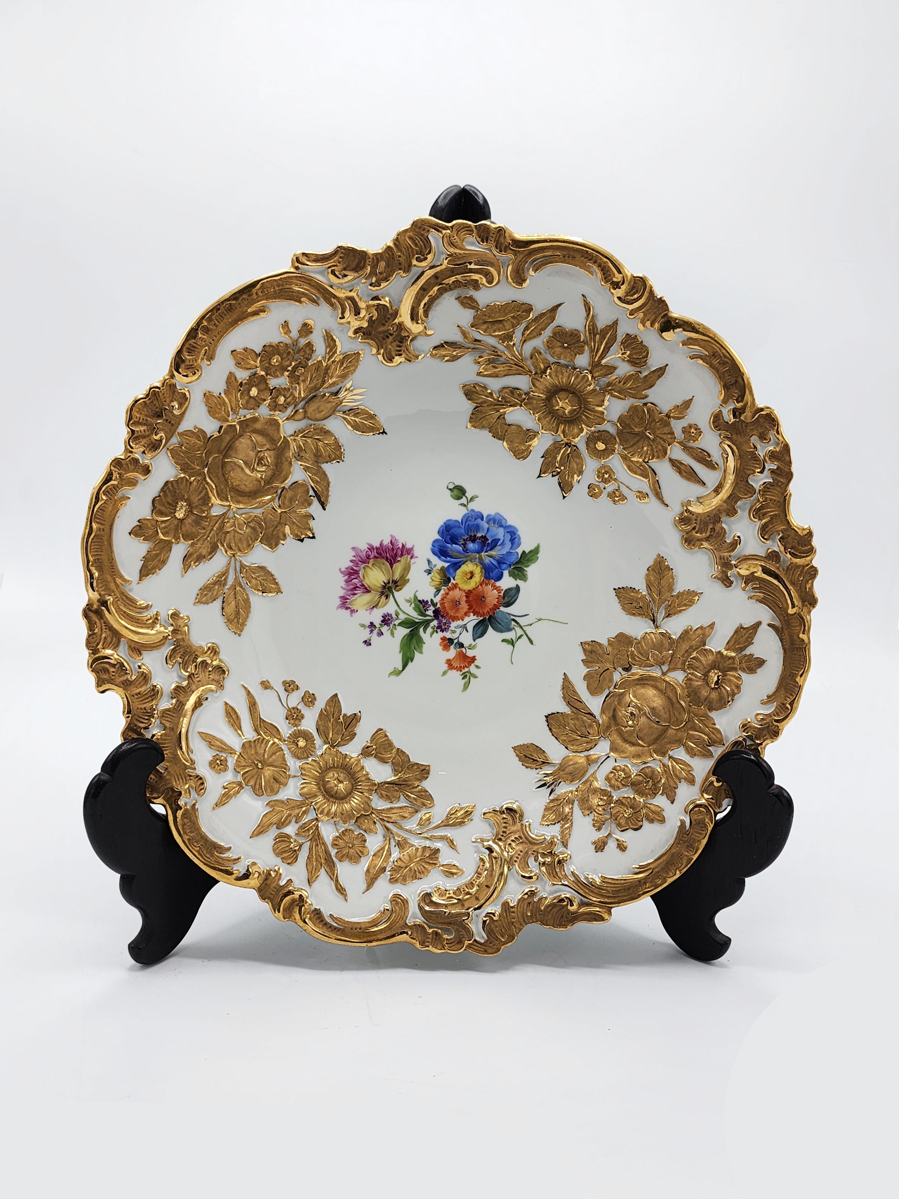 Assiette creuse en porcelaine de Meissen peinte à la main et dorée
Belle assiette creuse en porcelaine de Maissen dont le bord est orné de motifs dorés de fleurs et de feuilles. Au centre, peint à la main, se trouve une illustration de fleurs