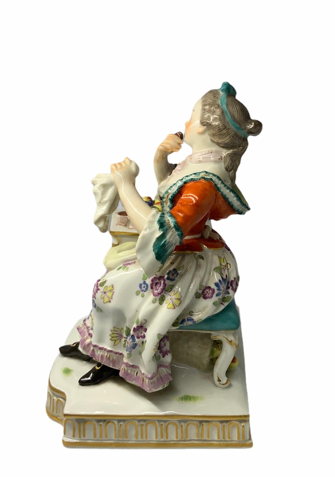 This a colorful and well made Meissen porcelain figurine that is part of group of five that represents the five senses. She represents the sense of taste. The porcelain figurine depicts a young lady sitting in front of a table with a plate of