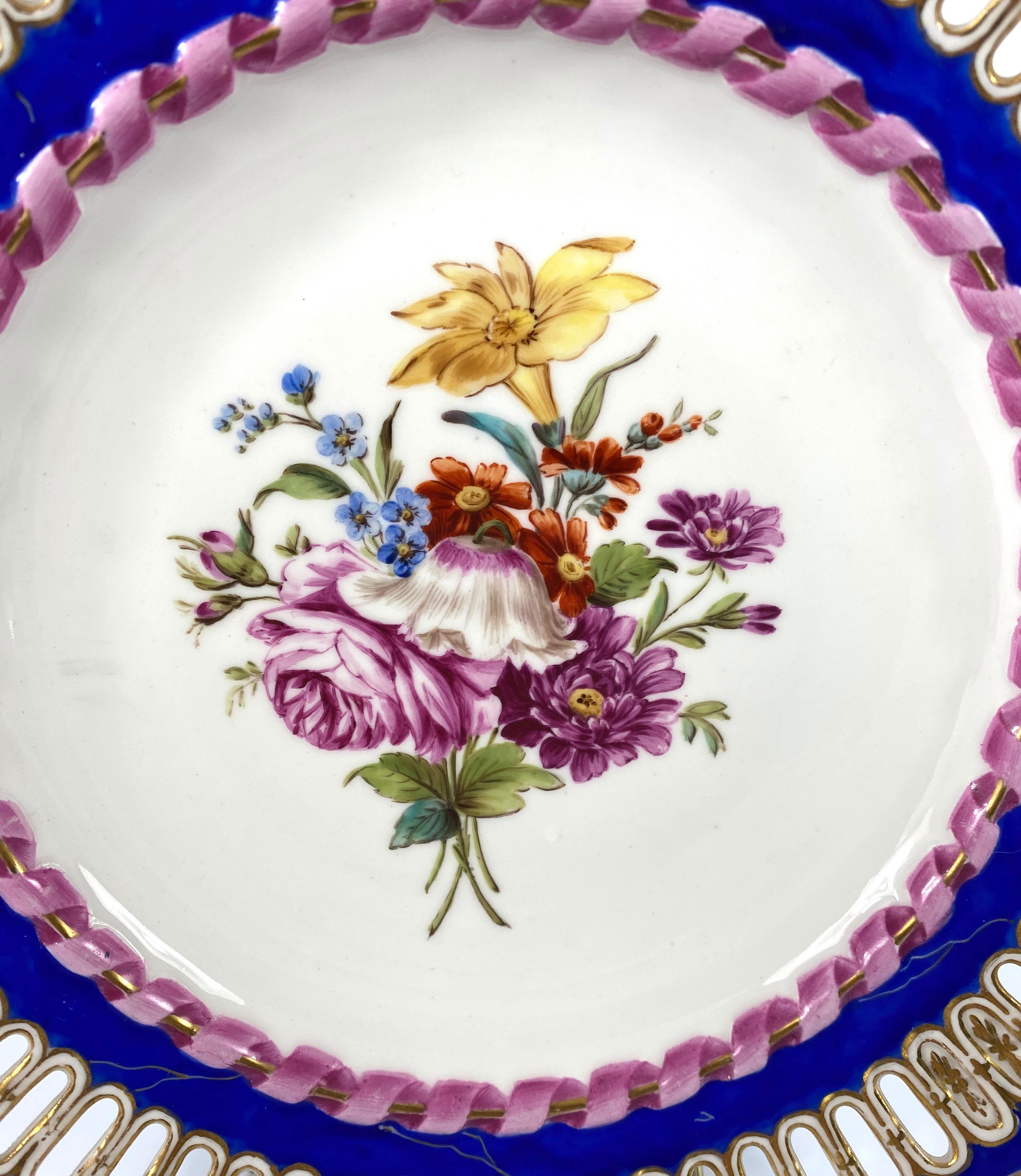 Meissen porcelain reticulated plate, circa 1850. Beautifully hand painted to the centre, with a spray of Spring flowers, within a moulded pink ribbon and gilt scroll border. The outer rim, pierced, and gilded, upon a gilt veined blue
