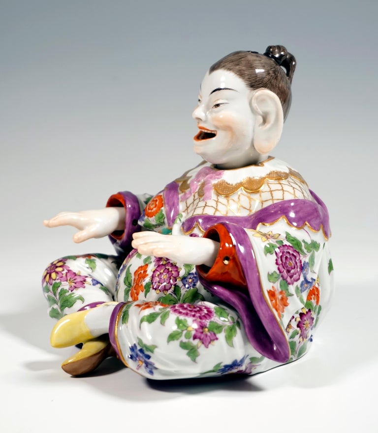 Depiction of a sitting, smiling Buddha figure from a series of folk types. Voluminous female body with hair strictly tied back and a wide robe sitting cross-legged, arms straight in front of her. Movable head, tongue and hands, detachable head with