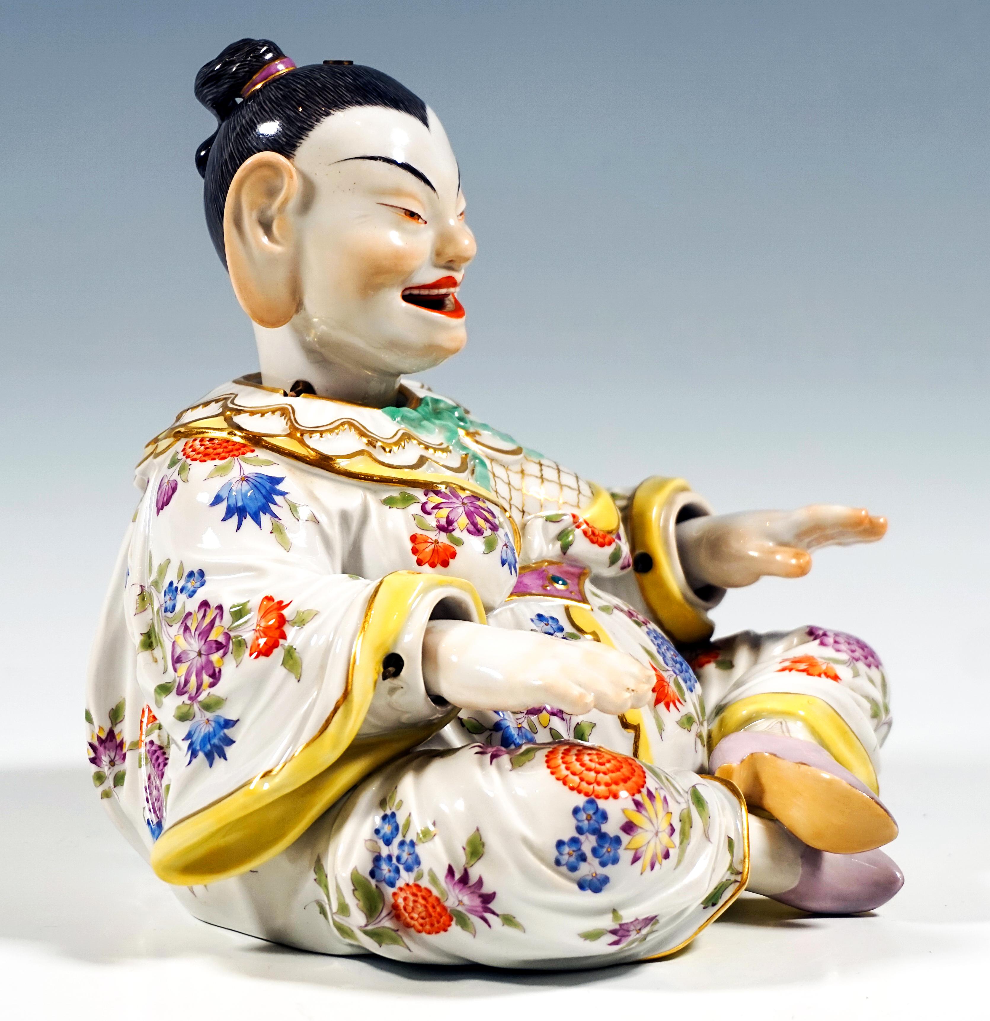 Depiction of a sitting, smiling female Buddha figure from a series of folk types. Voluminous body with hair strictly combed back and a wide robe sitting cross-legged, arms straight in front of her. Movable head, tongue and hands, 
detachable head