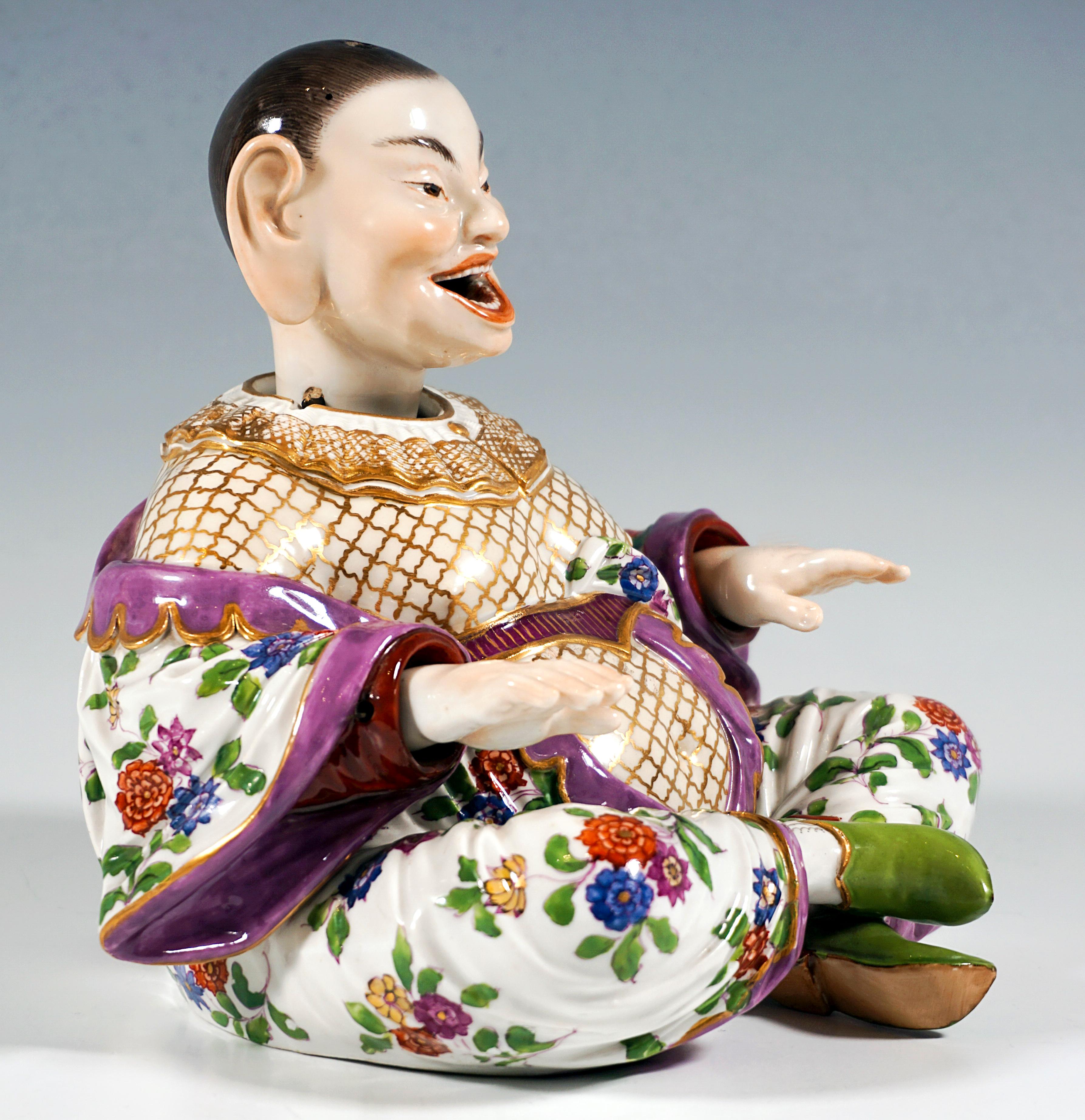 Depiction of a sitting, smiling Buddha figure from a series of folk types. Voluminous body with hair strictly combed back and a wide robe sitting cross-legged, arms straight in front of her. Movable head, tongue and hands, detachable head with metal