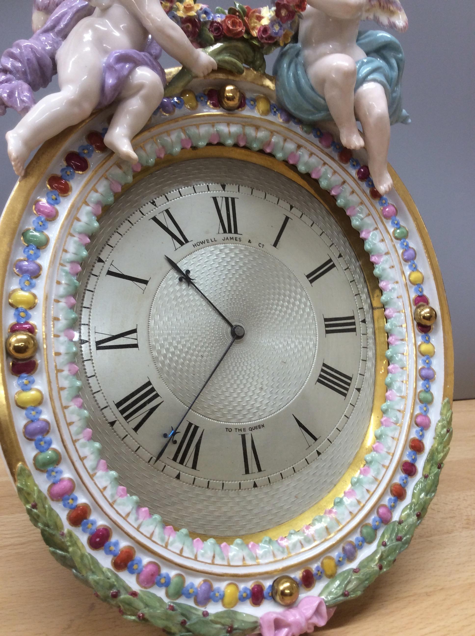 A Meissen porcelain oval shaped Strut clock with two putti and well modelled trailing flowers and wreath decoration. (The back of the case at 12 o’clock carrying the crossed swords mark for Meissen in a blue underglaze). 

 Beautifully engraved